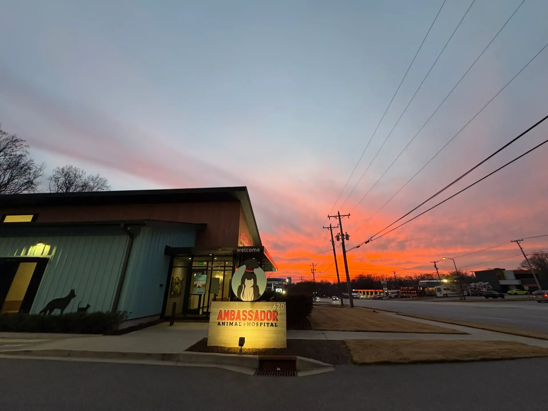 Modern storefront at dusk with warm lights and a slanted roof, set against a colorful sunset sky