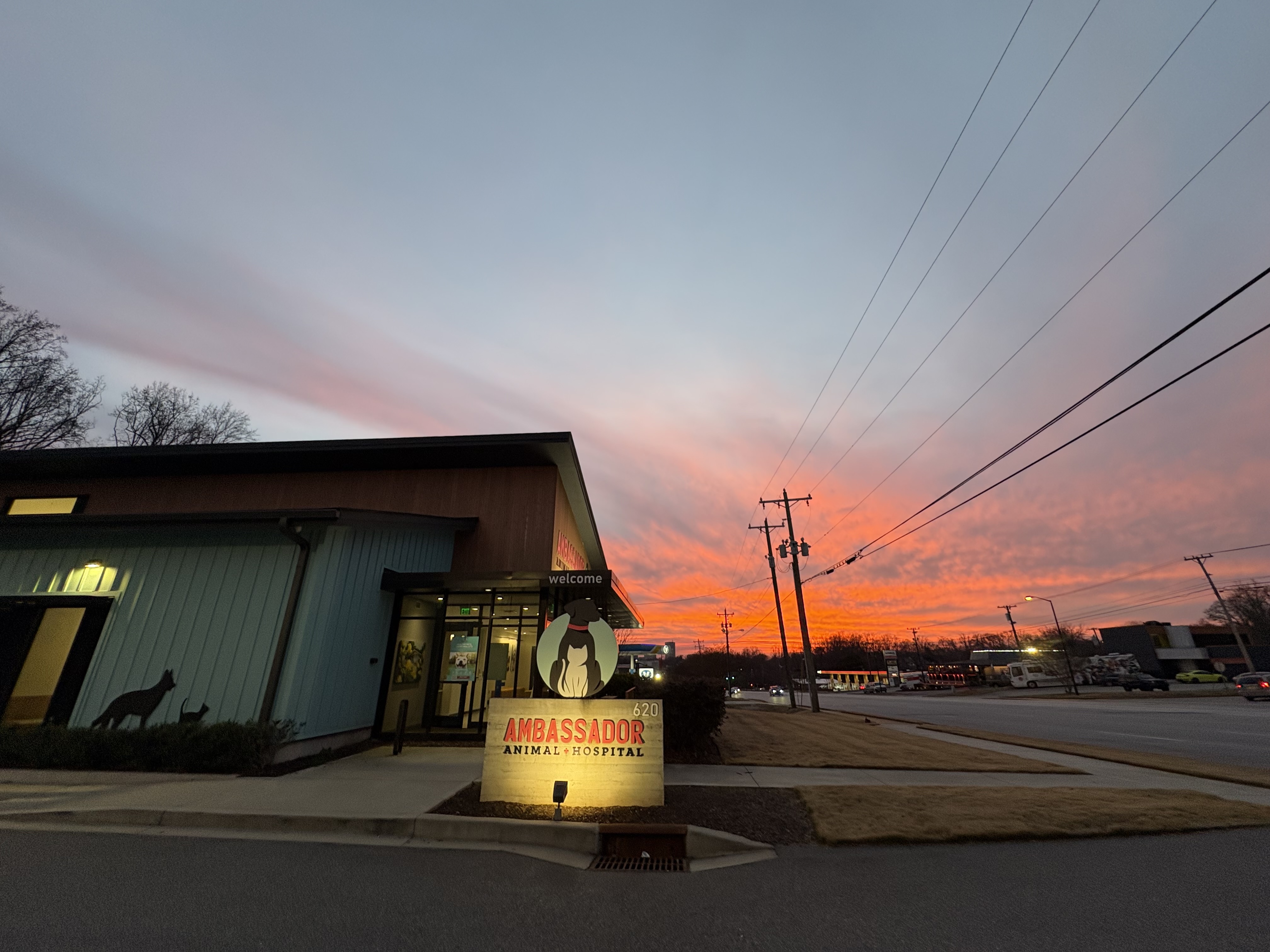 Modern storefront at dusk with warm lights and a slanted roof, set against a colorful sunset sky