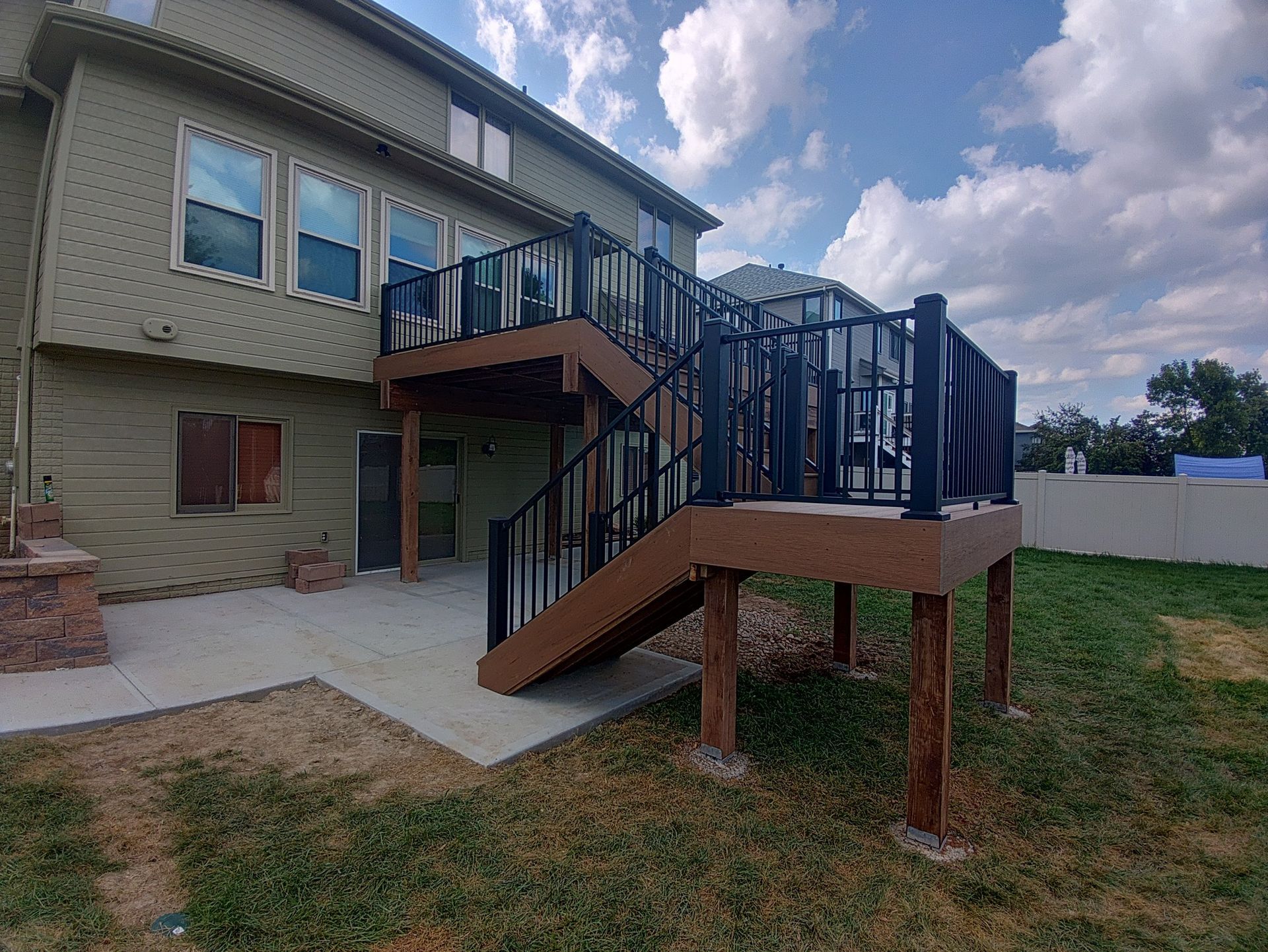 A raised deck with black railings and brown composite boards connected to a multi-story, olive-colored house.