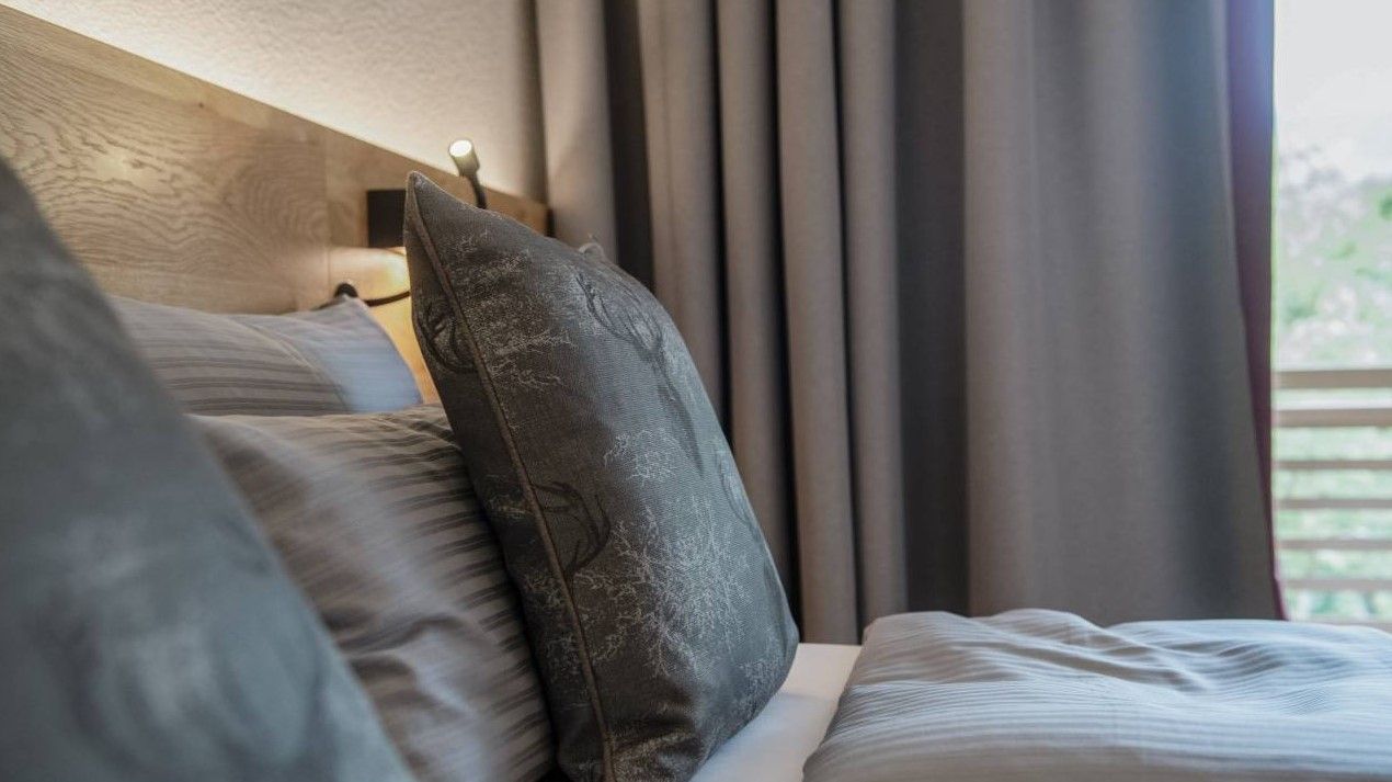 Ein Hotelzimmer mit einem Bett, Kissen, Vorhängen und einem Fenster.