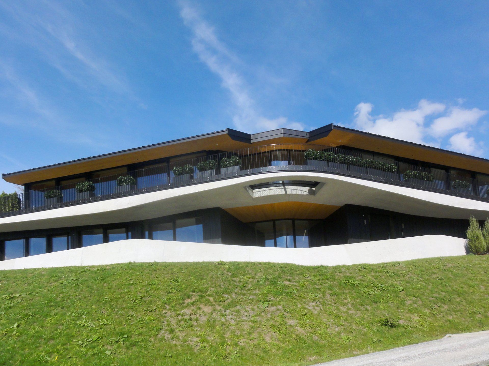 Ein großes Gebäude mit Balkon liegt auf einem grasbewachsenen Hügel