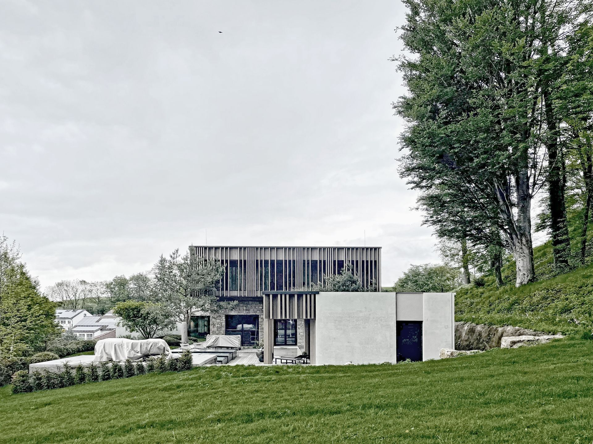 Auf einem grasbewachsenen Hügel steht ein Haus, umgeben von Bäumen.