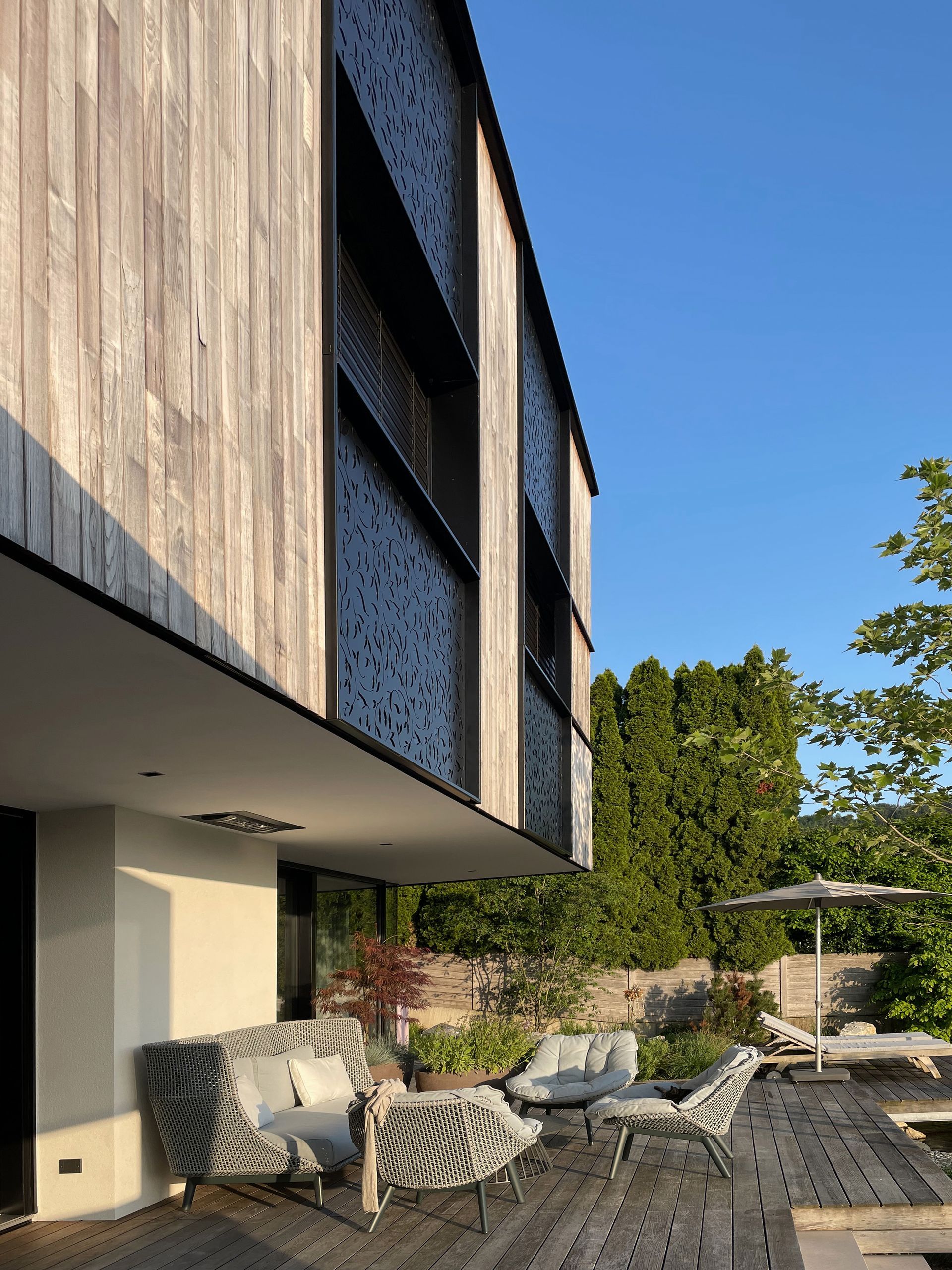Ein Haus mit Holzfassade und einer Terrasse mit Stühlen und Sonnenschirmen
