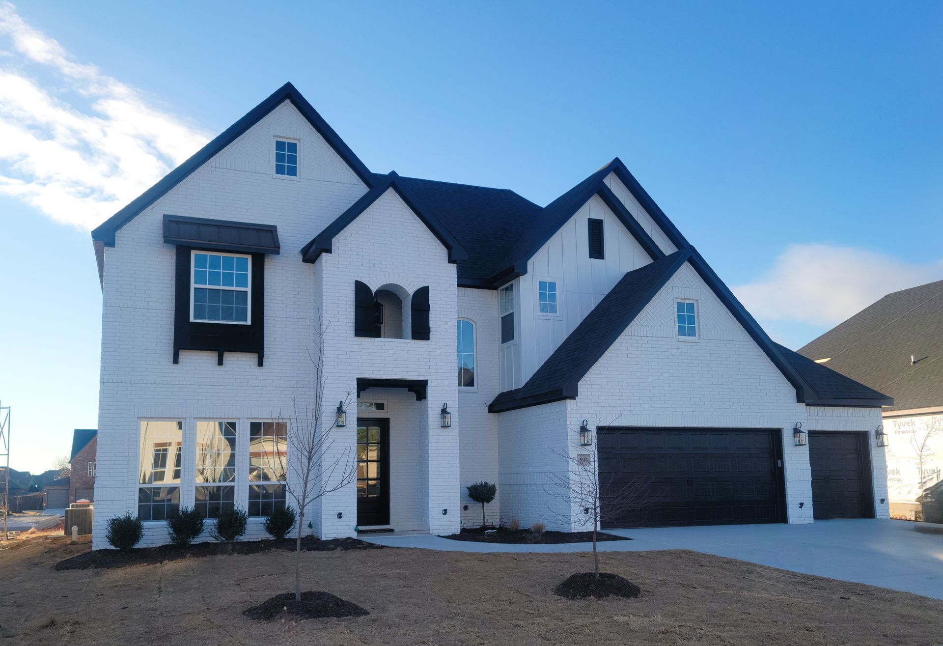 New white two-story house with black roof and garage under a clear blue sky