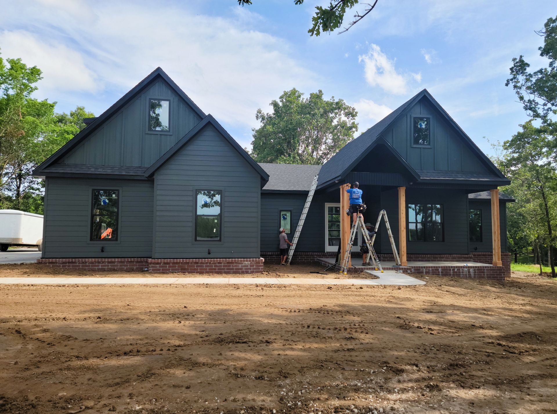 New dark-gray house with two gables; workers install a front porch during construction