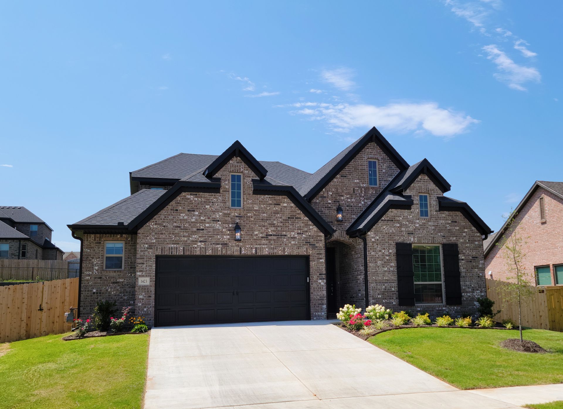 Brick suburban house with black garage door, stone facade, and a front lawn under a blue sky