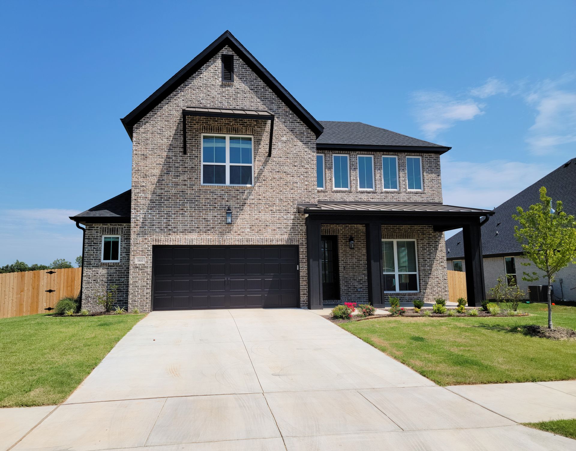 Modern two-story brick house with black garage doors and a wide concrete driveway under a blue sky
