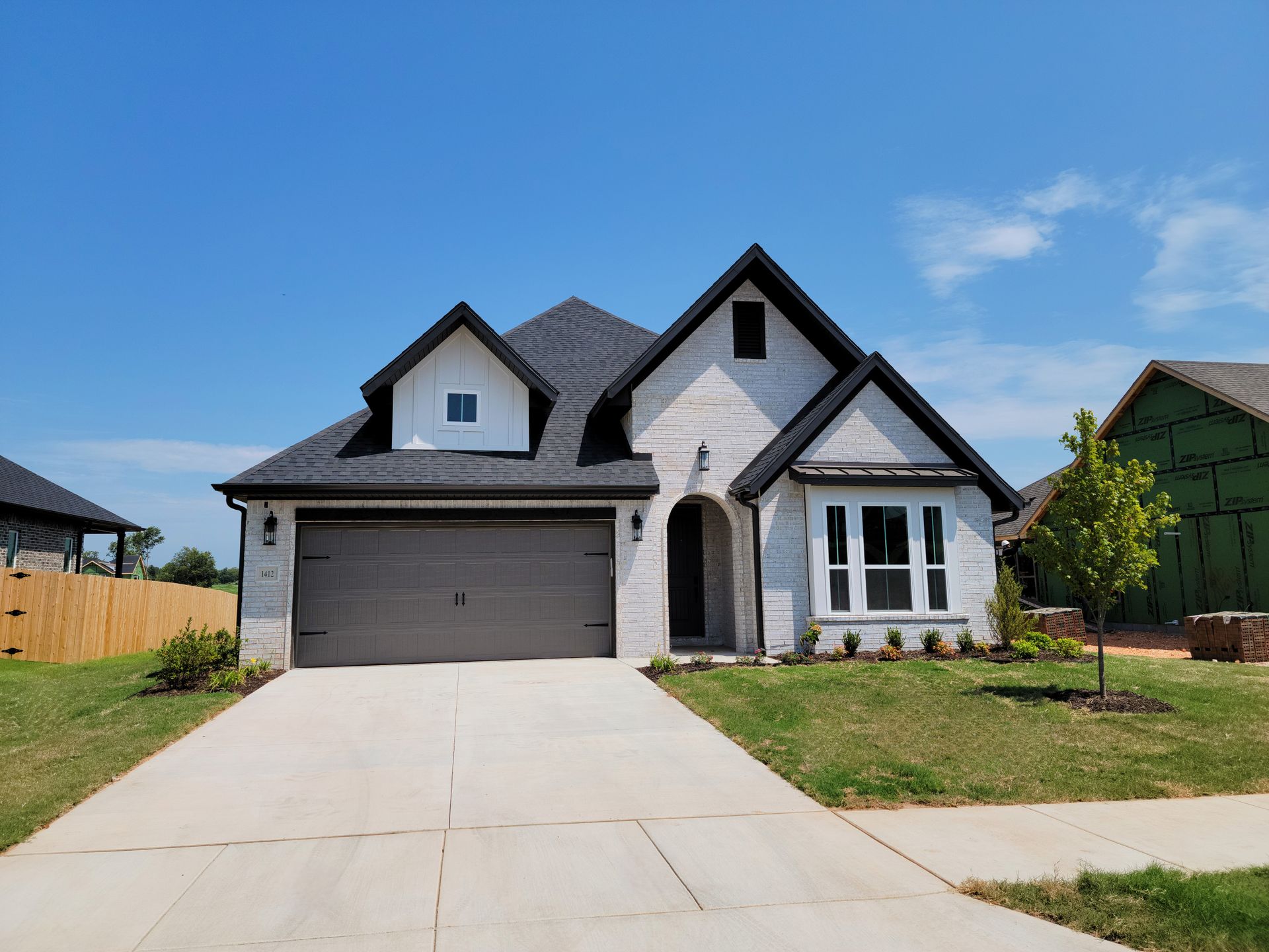 Suburban house with gray garage, white siding, and a concrete driveway under a blue sky