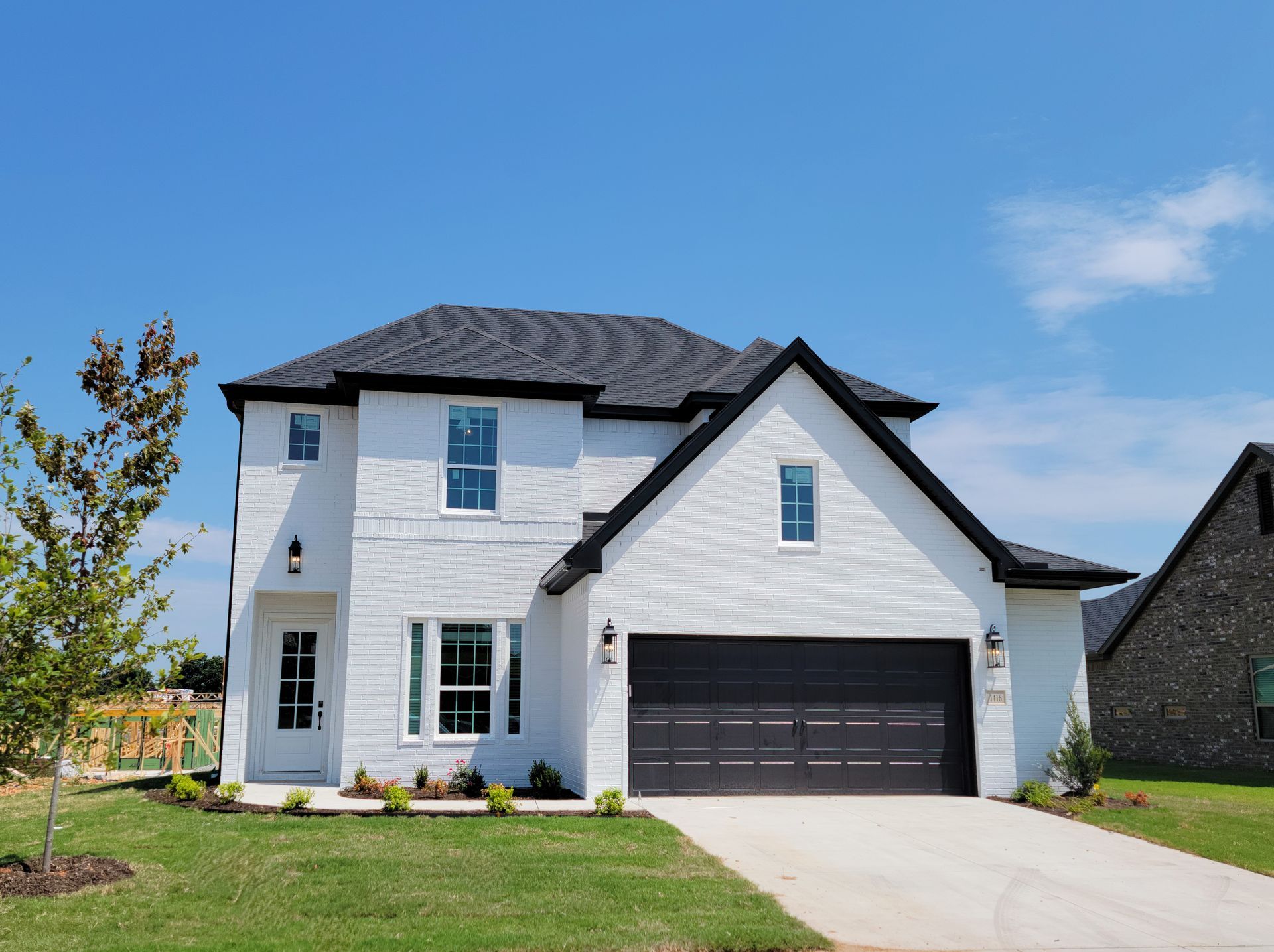 Modern white suburban house with dark roof, double garage, and a driveway under a blue sky