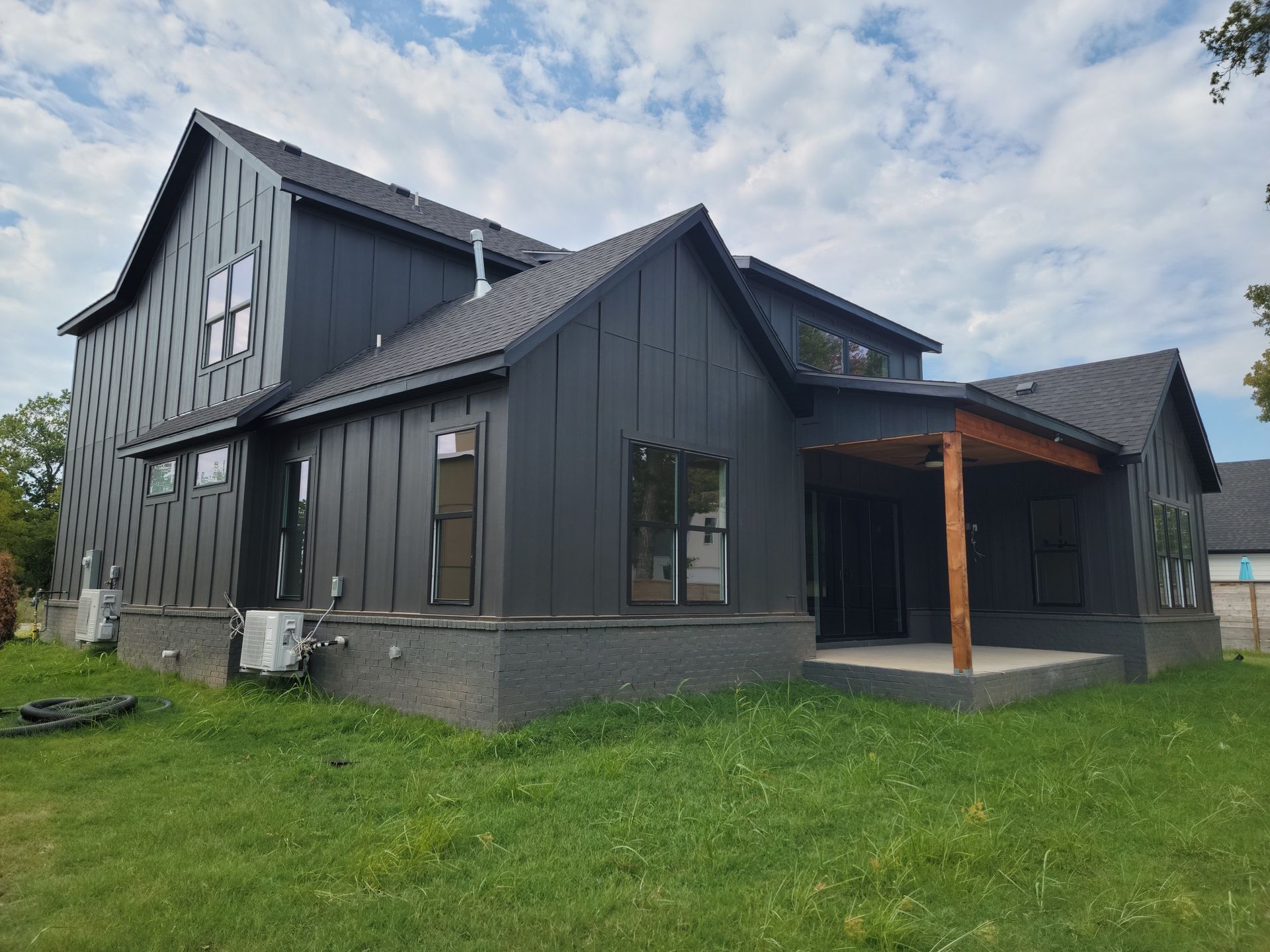 Dark gray modern house with wood-accent porch and green lawn under a cloudy sky
