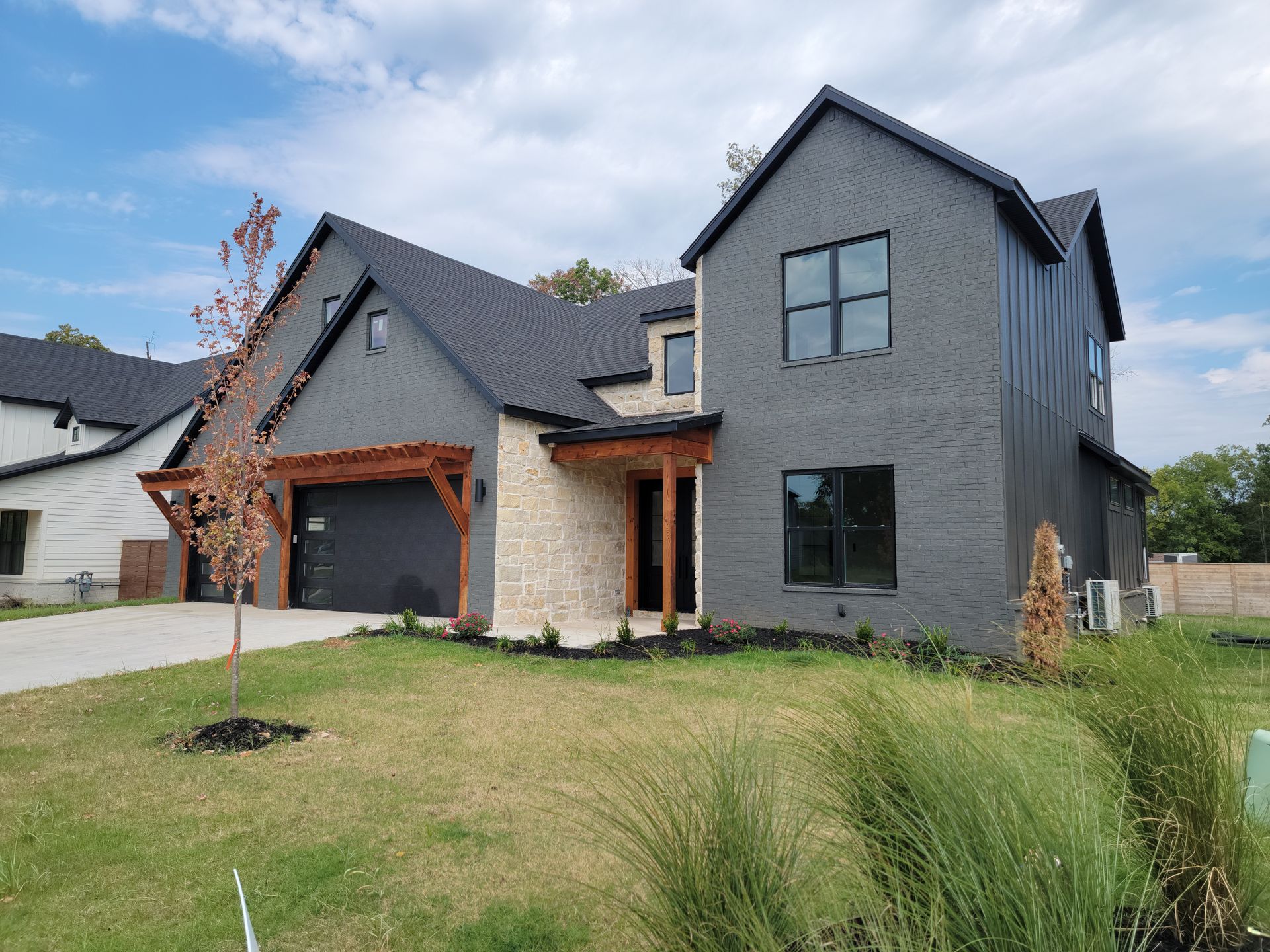 Modern dark gray house with steep roof, large windows, garage, and front lawn under a blue sky