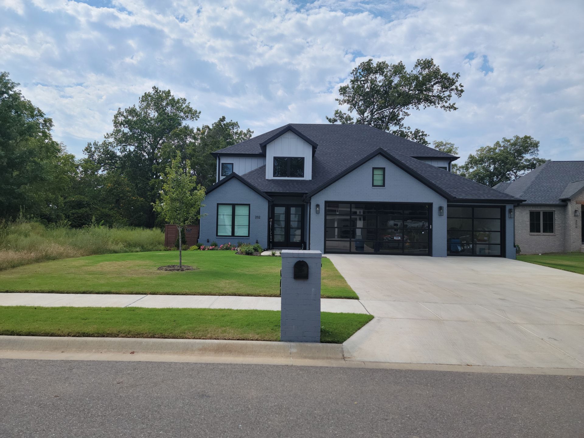 Suburban house with dark gray siding, two-car garage, driveway, and mailbox beside a grassy lawn