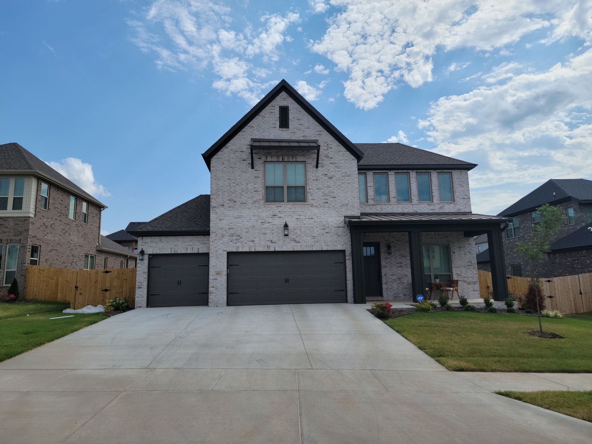 Two-story stone suburban house with a three-car garage and a wide concrete driveway under a blue sky