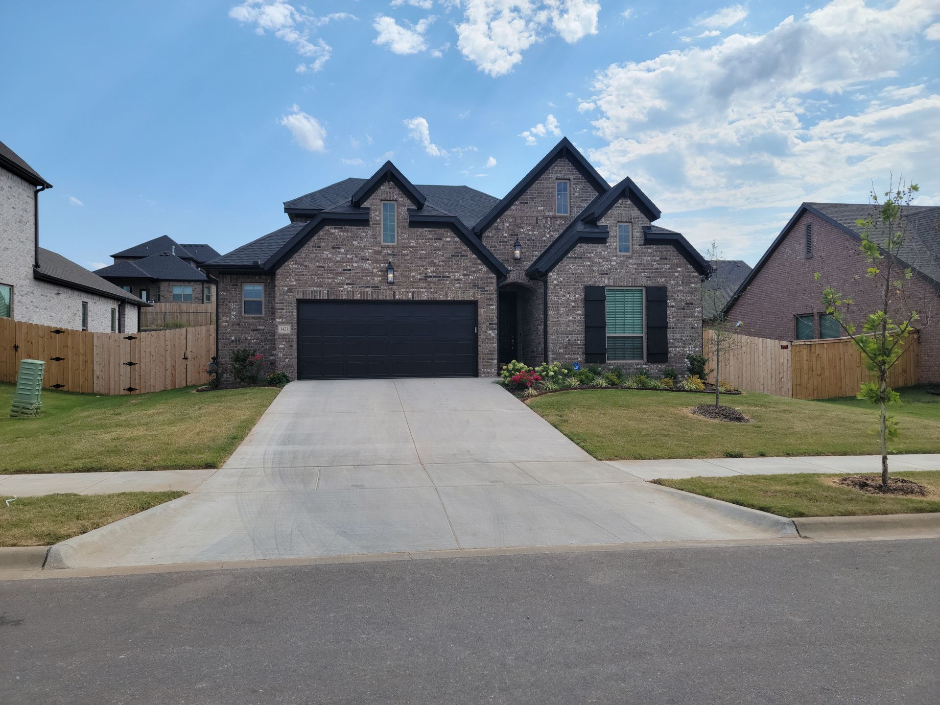 Suburban brick house with a dark garage, concrete driveway, and small front lawn under a blue sky
