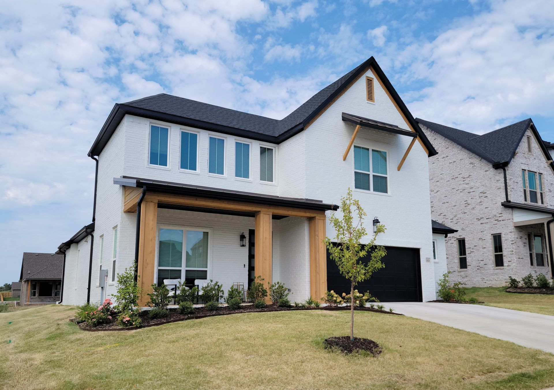 Modern white two-story house with black roof, large windows, and a front porch on a landscaped lawn.