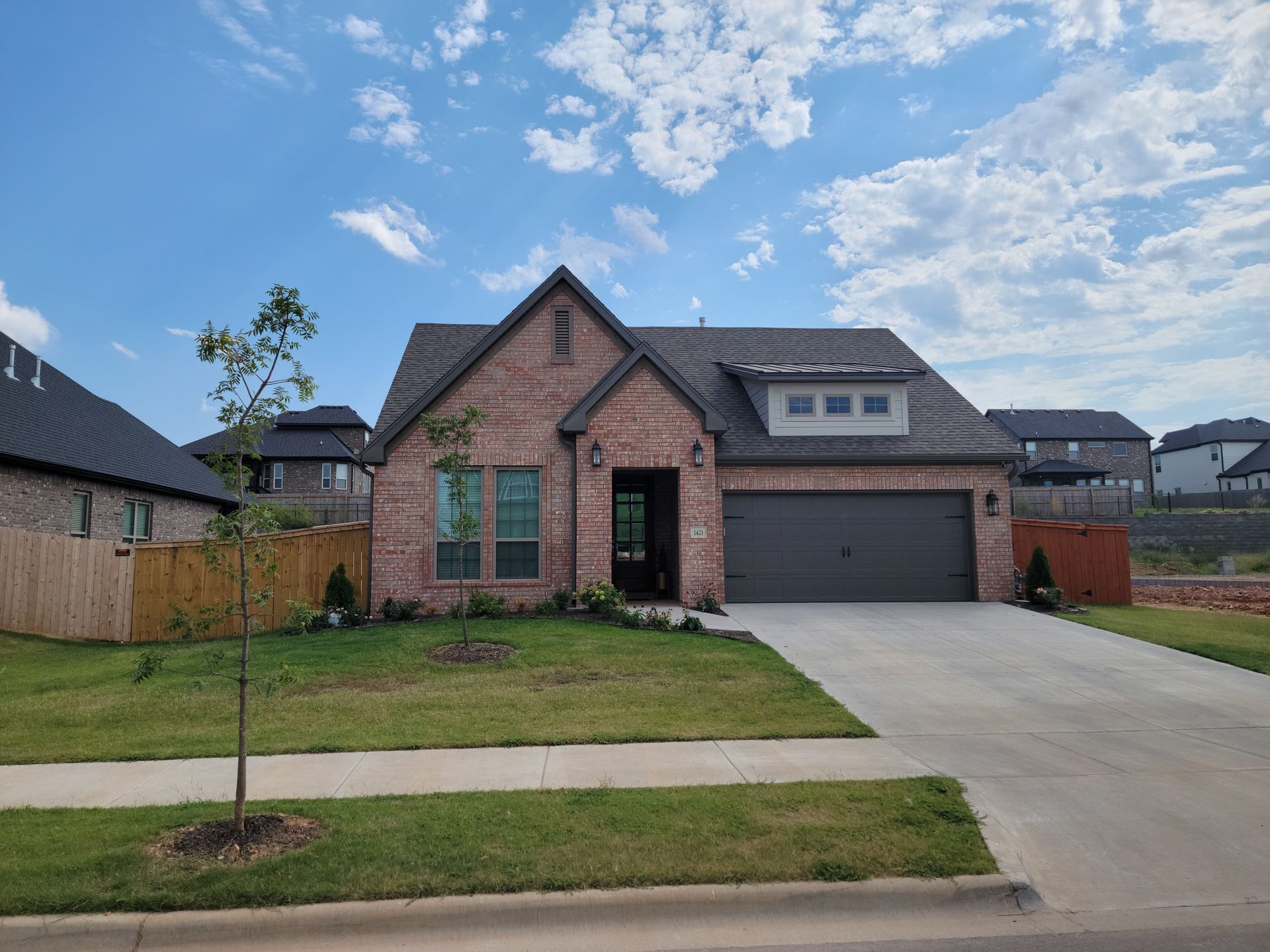 Brick single-story suburban house with a two-car garage and concrete driveway under a partly cloudy sky