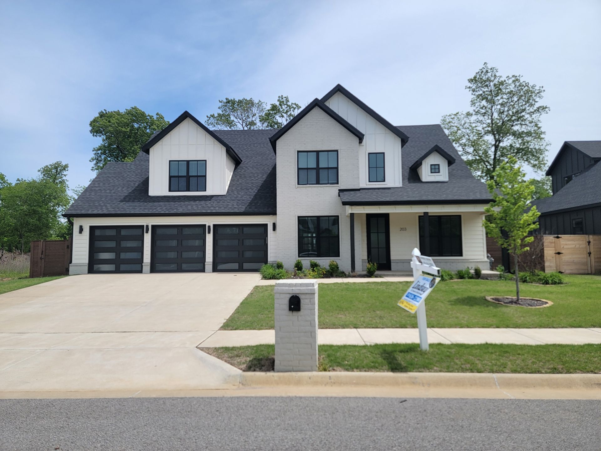 Modern two-story gray house with black garage doors, front lawn, and driveway in a suburban neighborhood