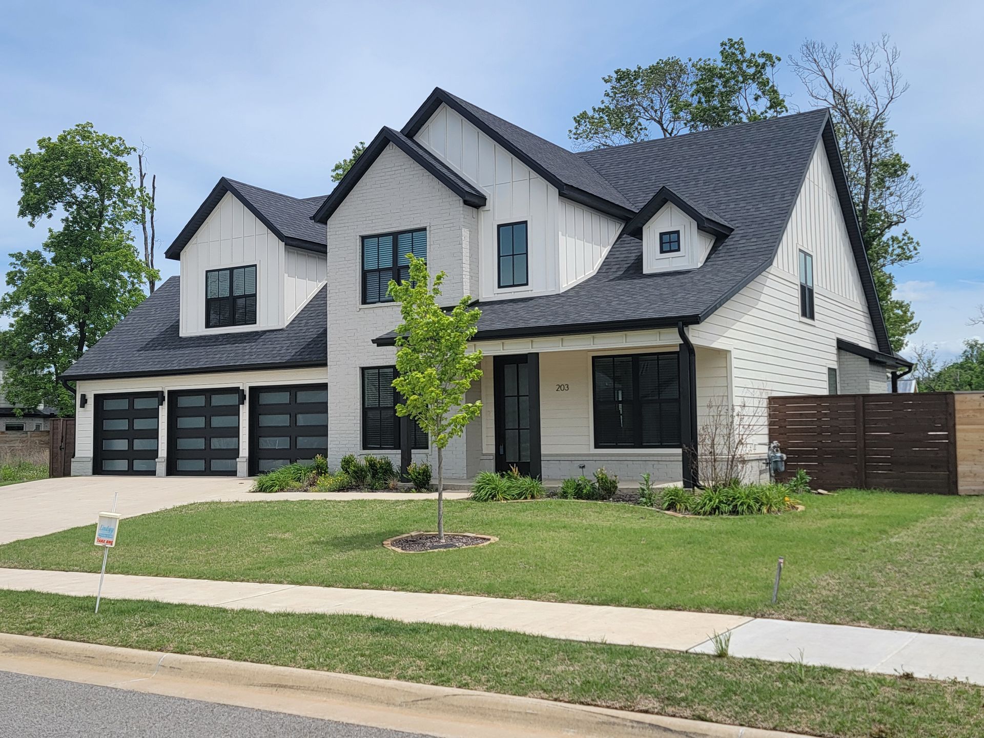 Large modern two-story white house with dark trim, front lawn, and three-car garage under a cloudy sky