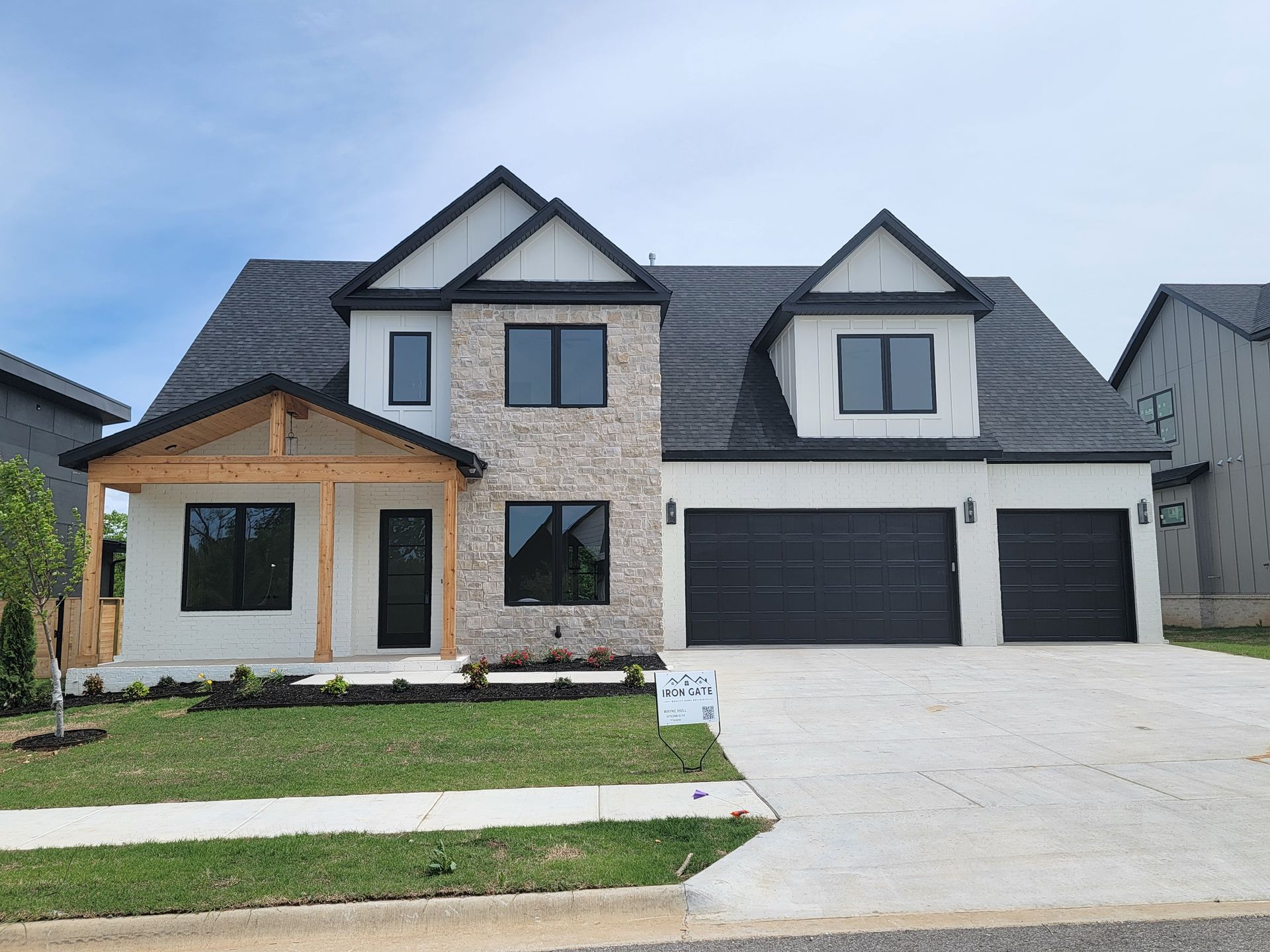 Modern two-story house with gray siding, black garage doors, and a stone-and-wood front facade