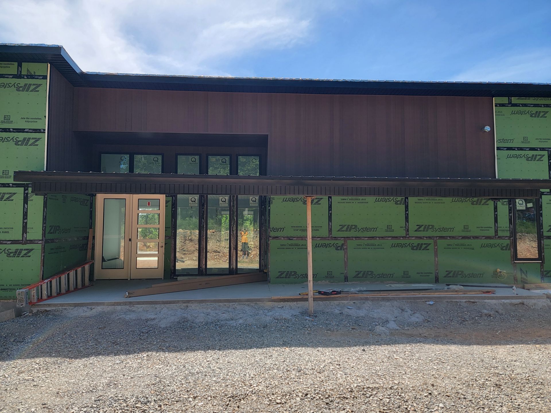 Partially built building with green insulated walls and a covered front entry under a blue sky