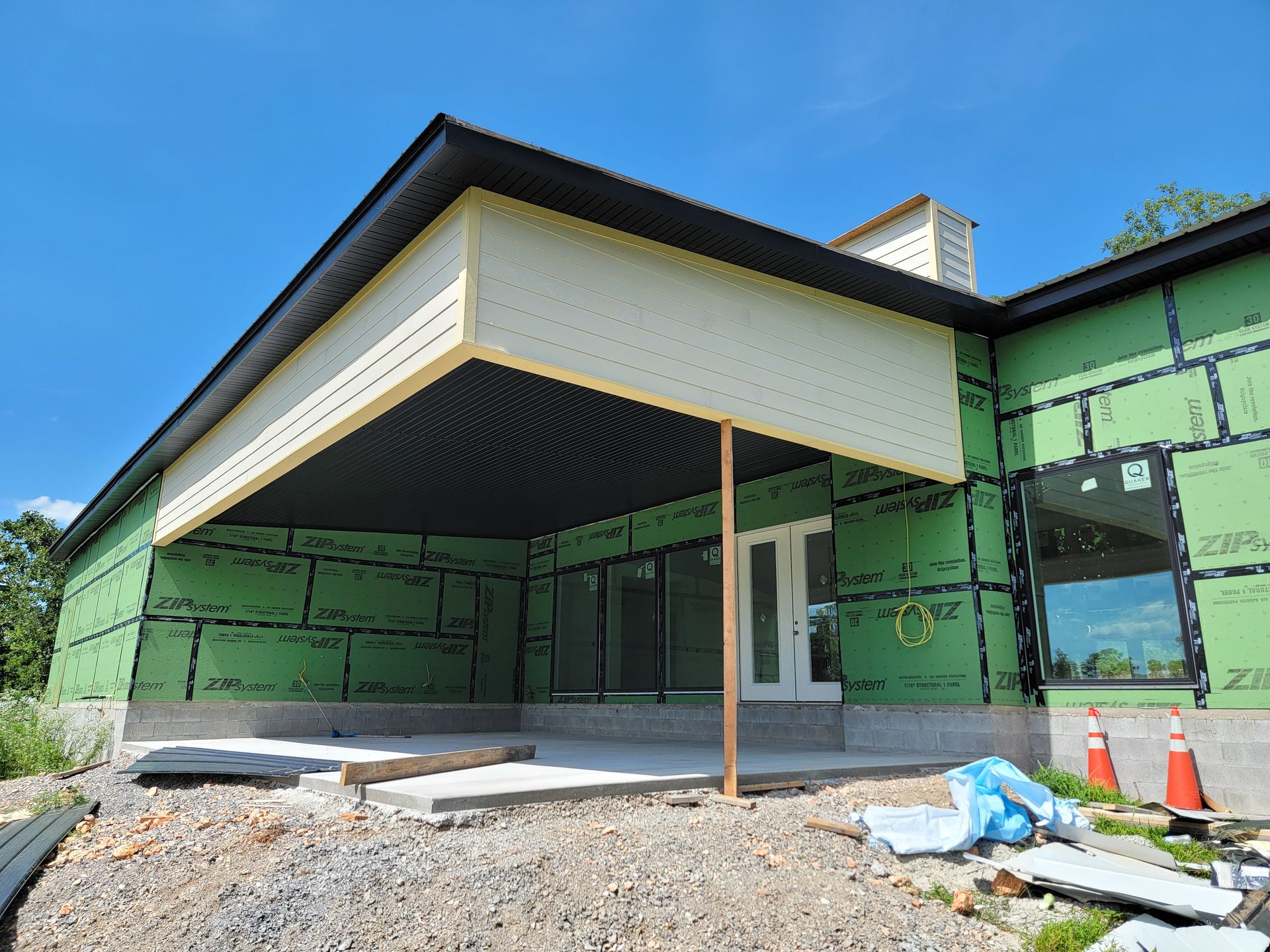 Covered porch addition on a house under construction, with green house wrap and exposed framing.