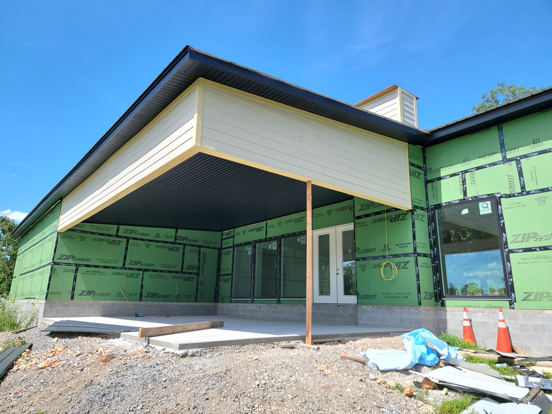 Partially constructed house exterior with green wrapped walls, a covered porch, and scattered building materials