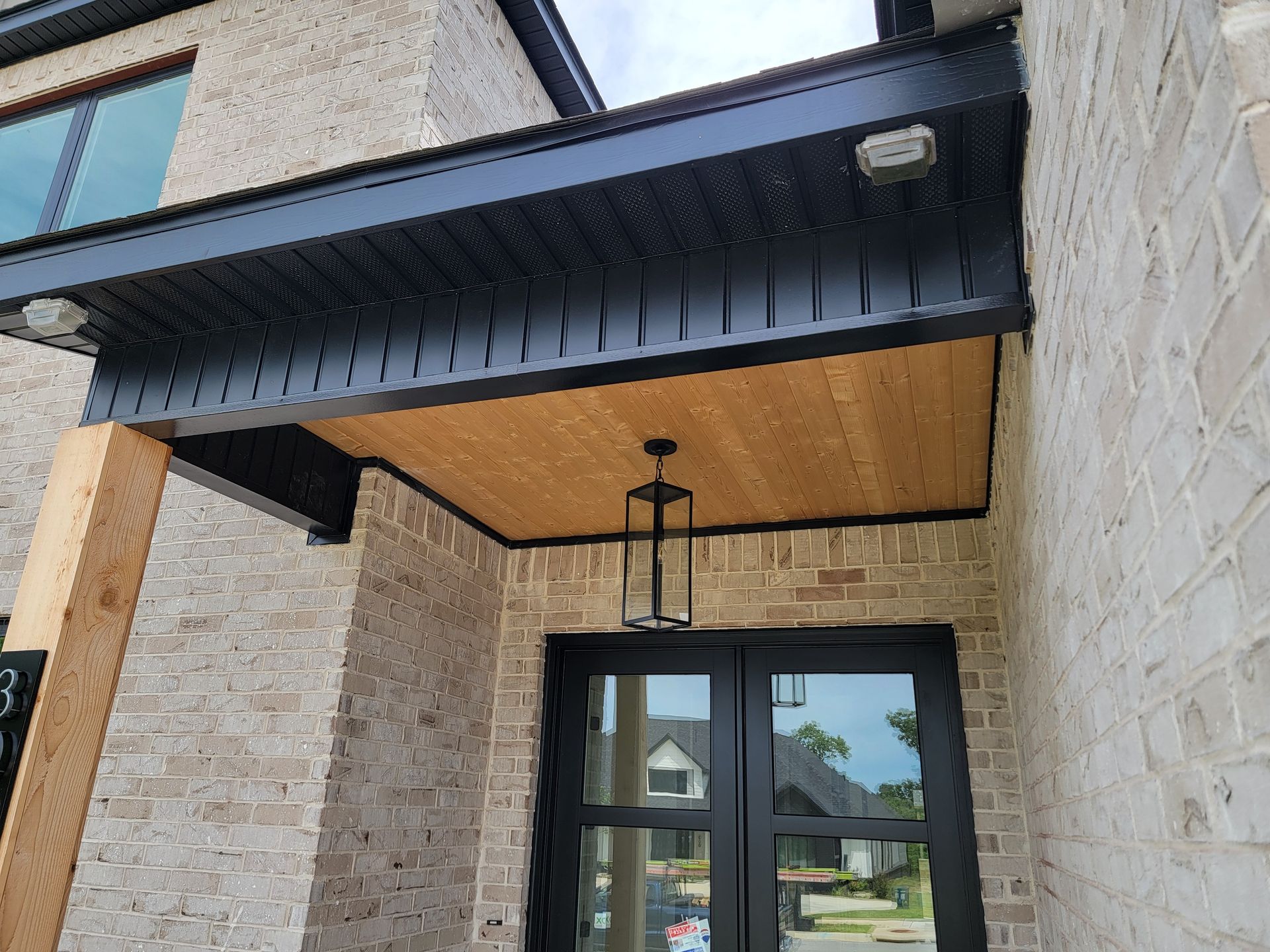 Modern townhouse entrance with black awning, wood soffit, glass door, and stone exterior.