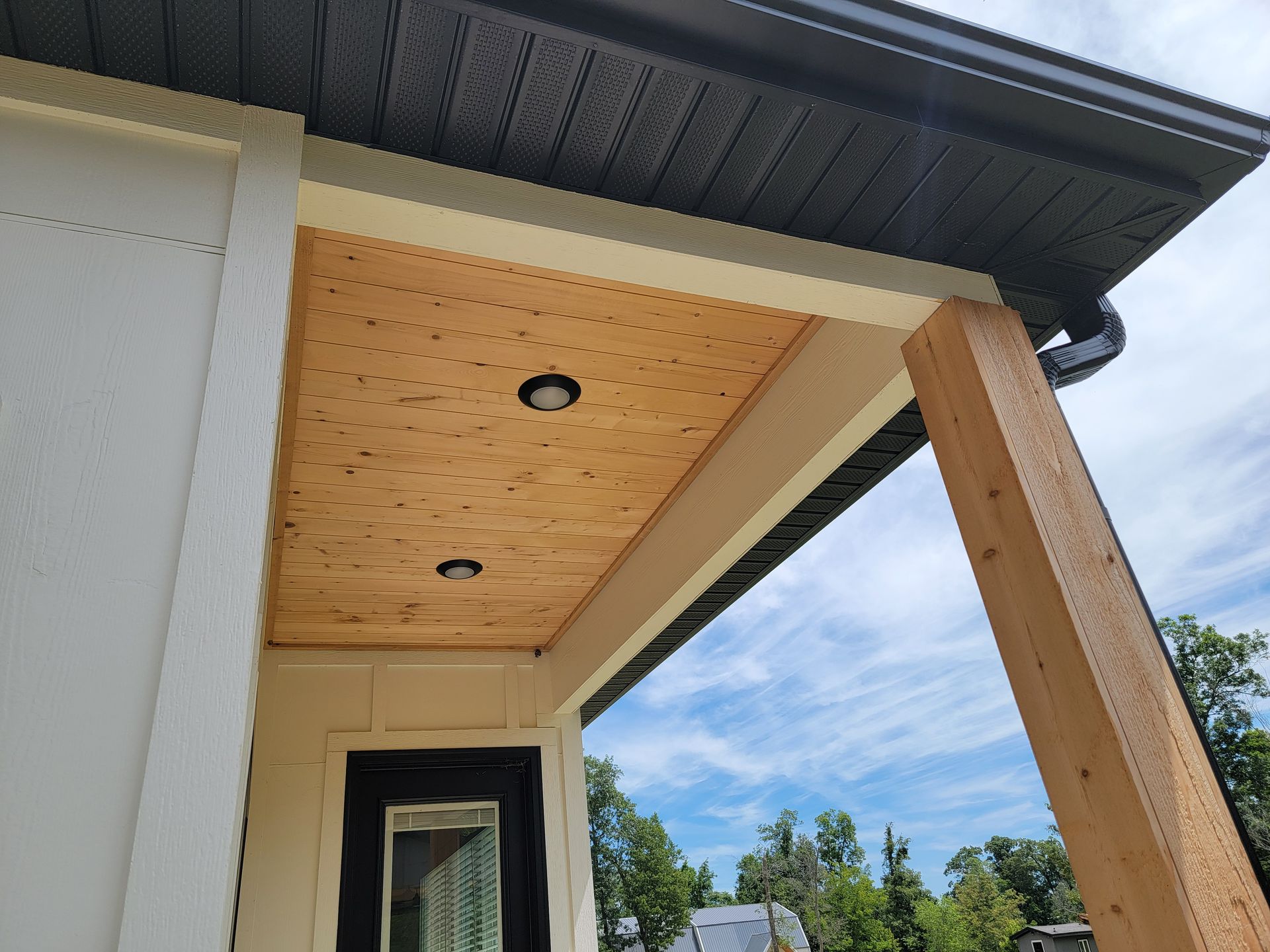 Front porch soffit with recessed lights, white siding, wood trim, and blue sky beyond.