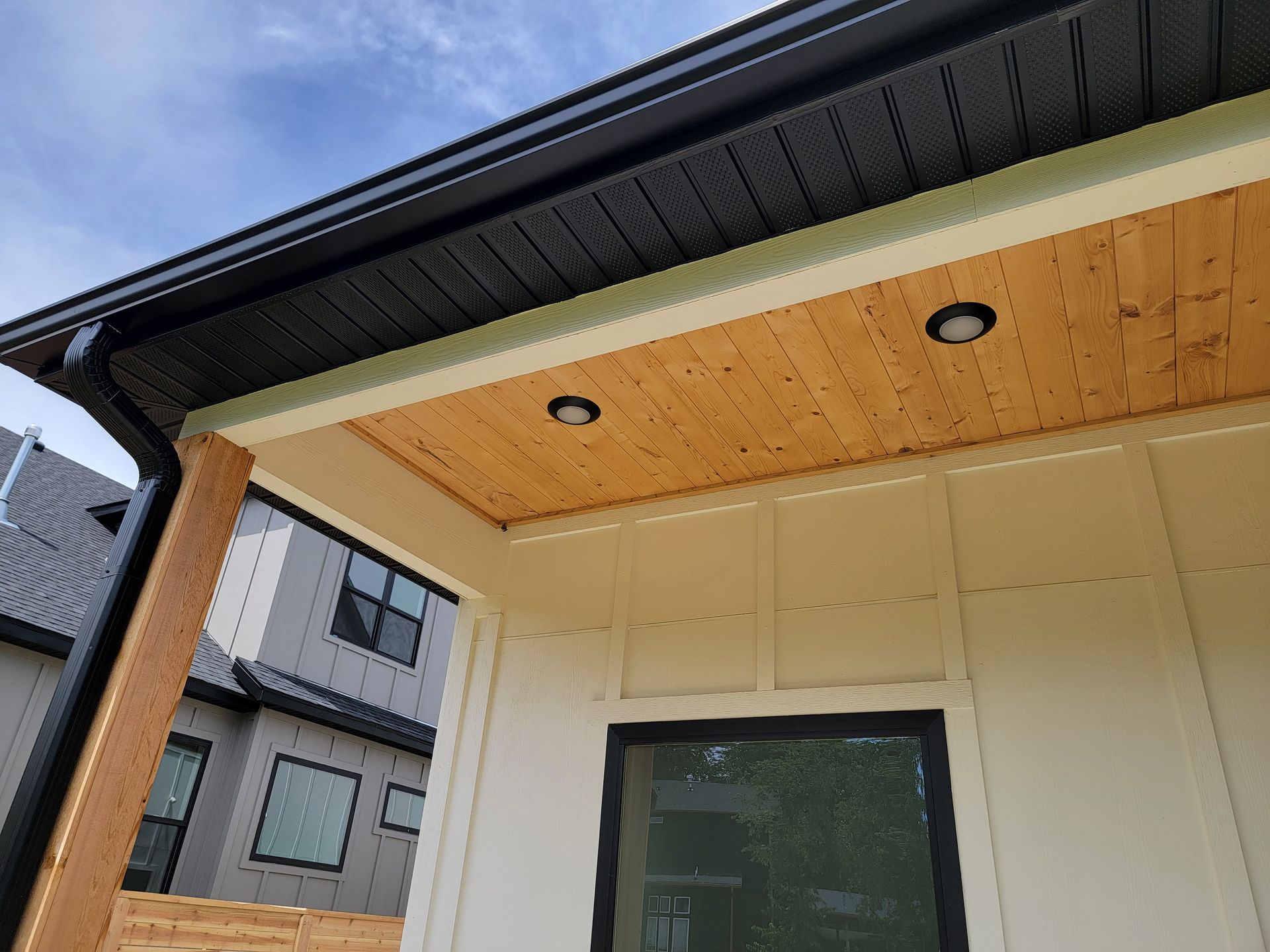 Modern house exterior with wooden soffit, recessed lights, and dark roof over a porch entrance