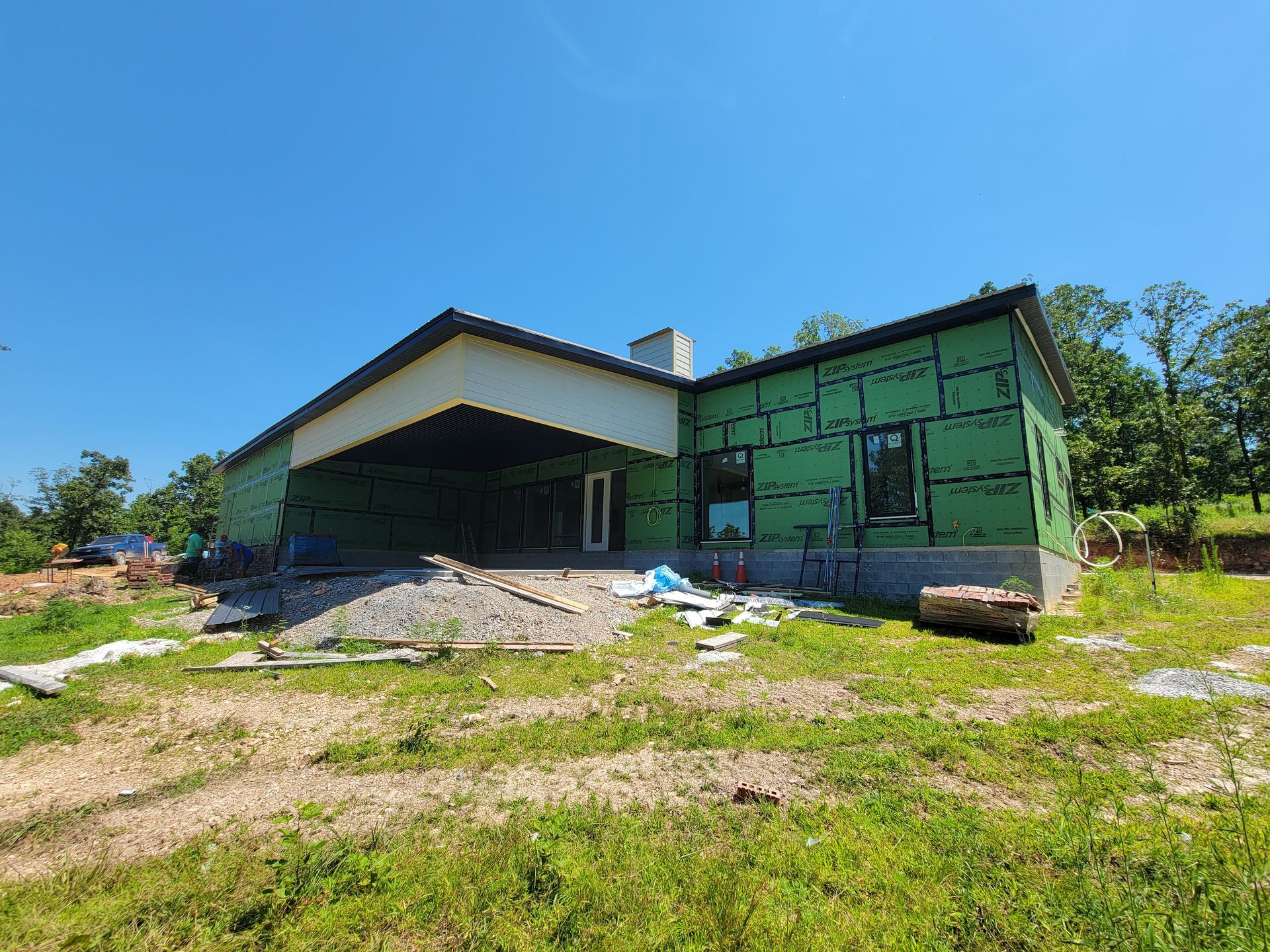 Partially built house with green exterior walls and a dirt yard under a blue sky