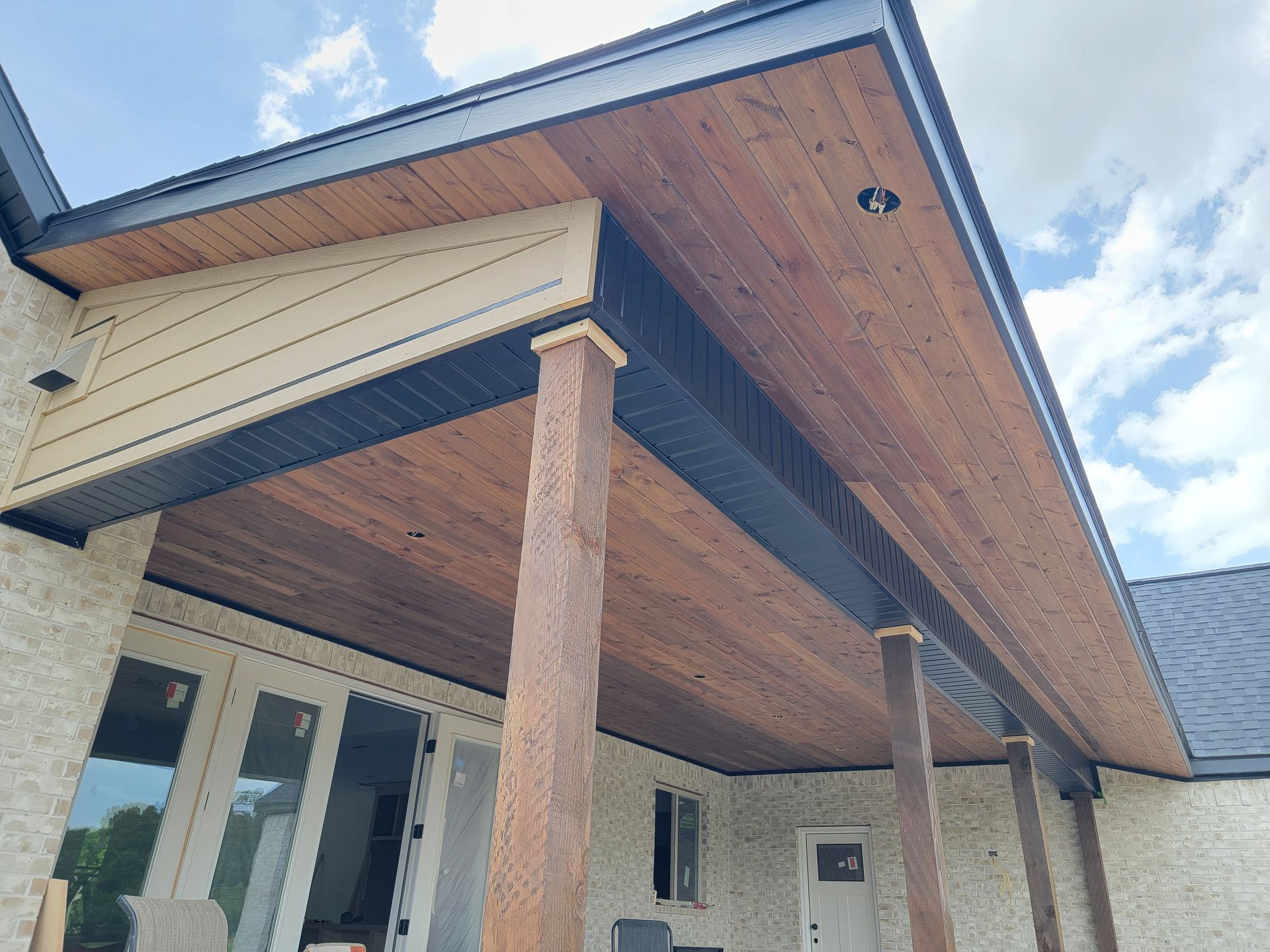 Covered porch with wood ceiling, brick columns, and white house siding under a cloudy sky