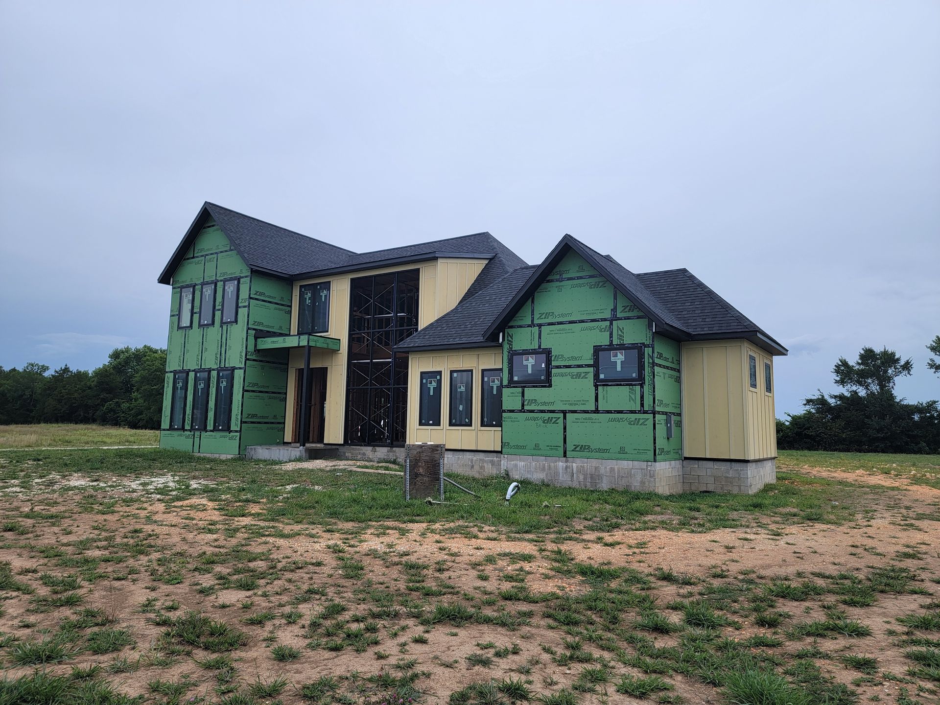 Partially built green house with dark roof on a sandy lot under an overcast sky