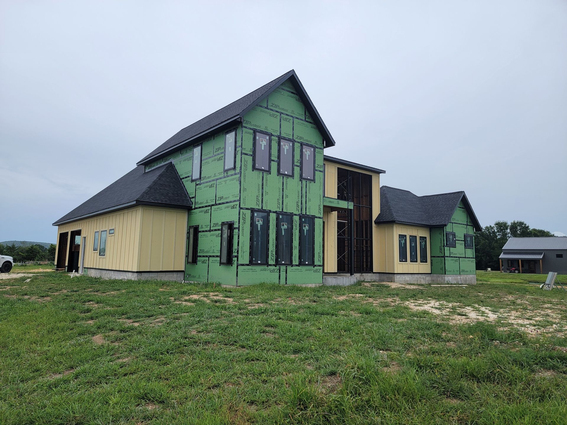 Partially finished house with green sheathing and black roof on a grassy lot under a cloudy sky