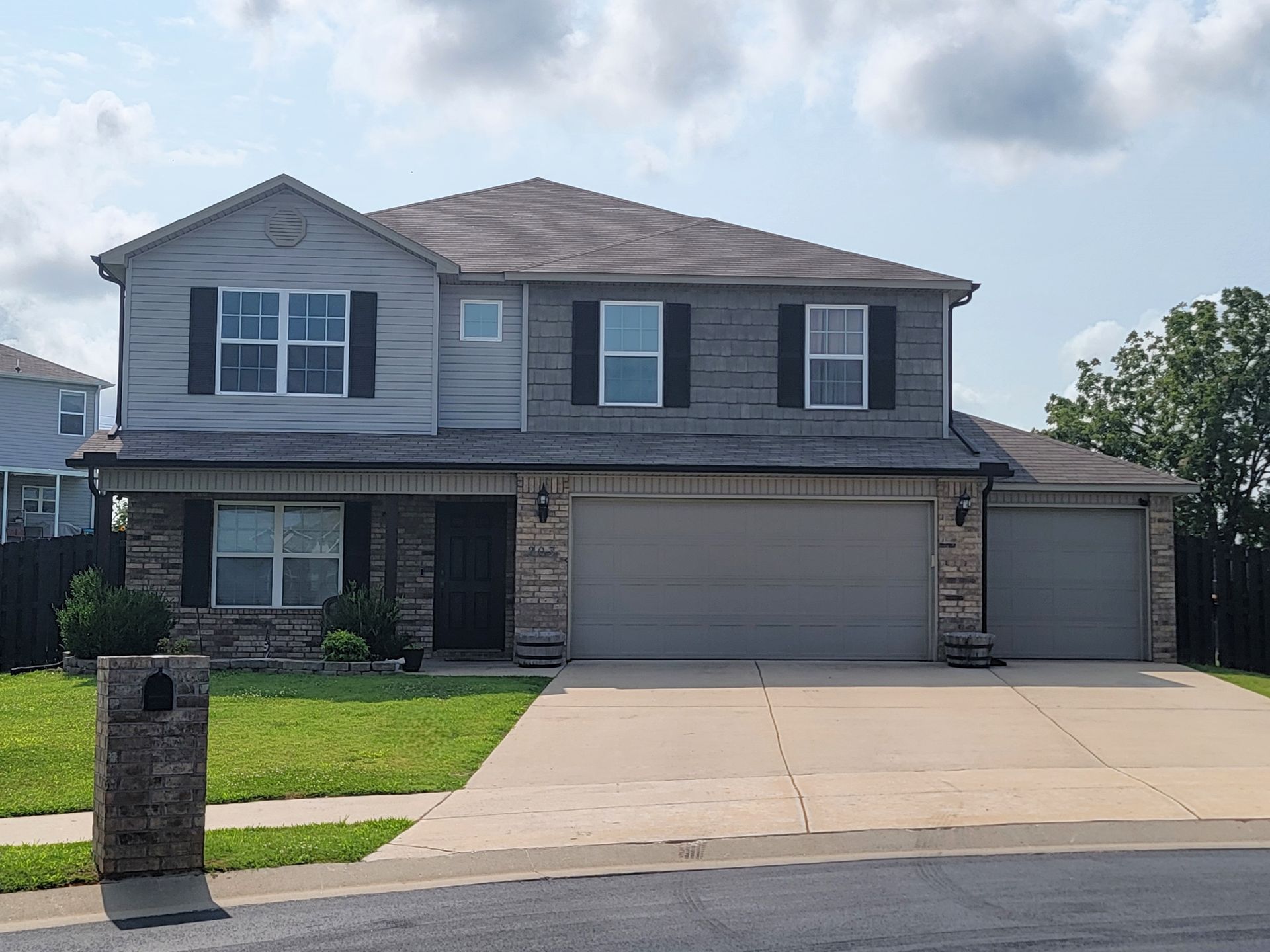 Two-story gray suburban house with a driveway, front lawn, and attached garage on a sunny day