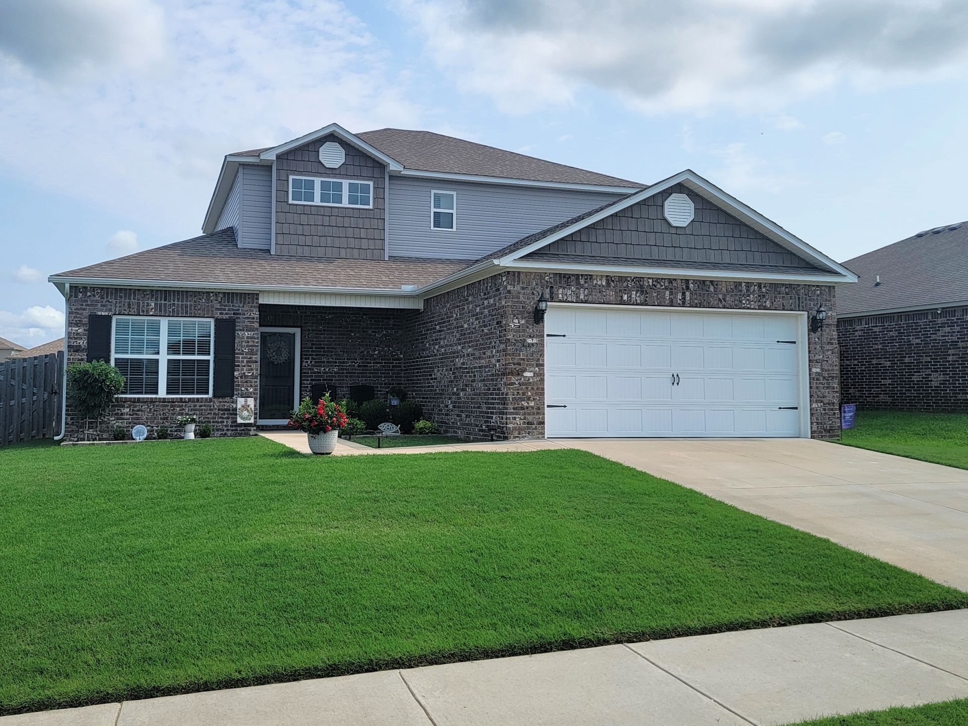 Suburban brick house with a white garage, green lawn, and driveway under a cloudy sky