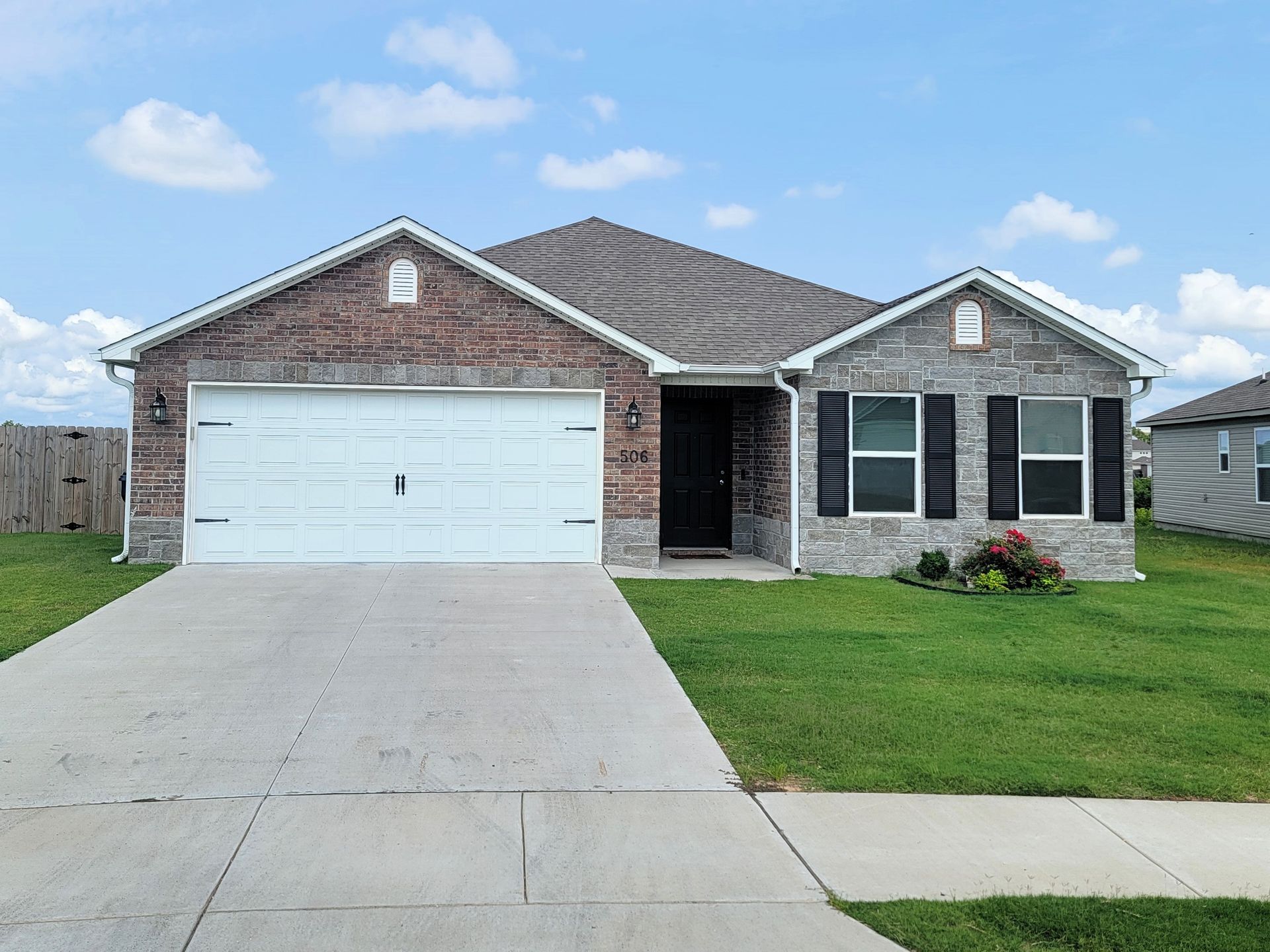 Suburban brick house with white garage, driveway, and green lawn under a blue sky