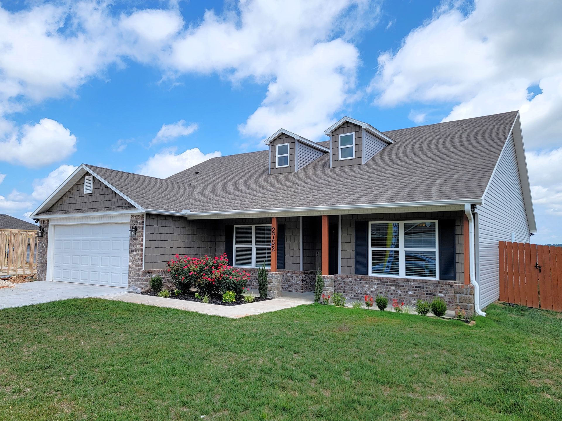 Single-story house with gray roof, brick and siding exterior, white garage, and green lawn under a blue sky