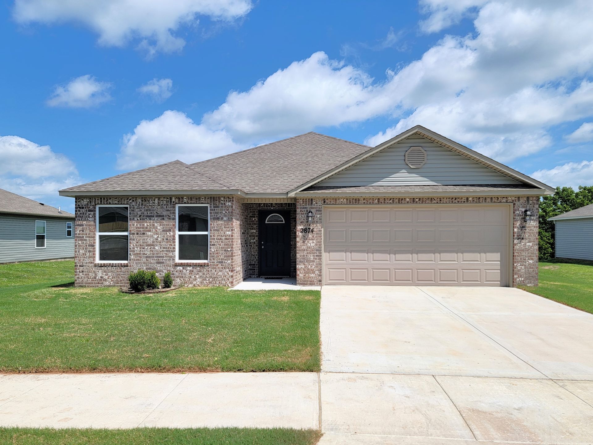Single-story brick house with two-car garage, front lawn, and driveway under a blue sky