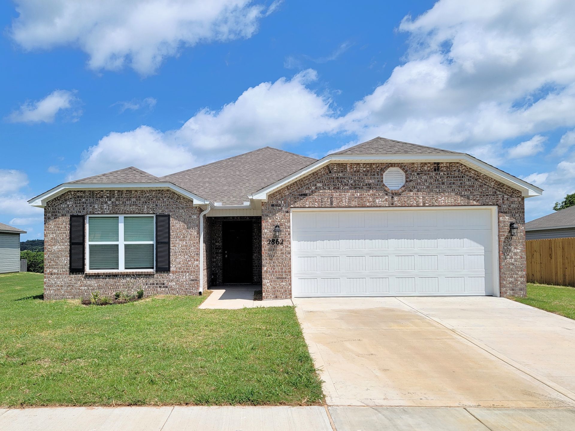 Single-story brick house with white garage door, front lawn, and driveway under a blue sky