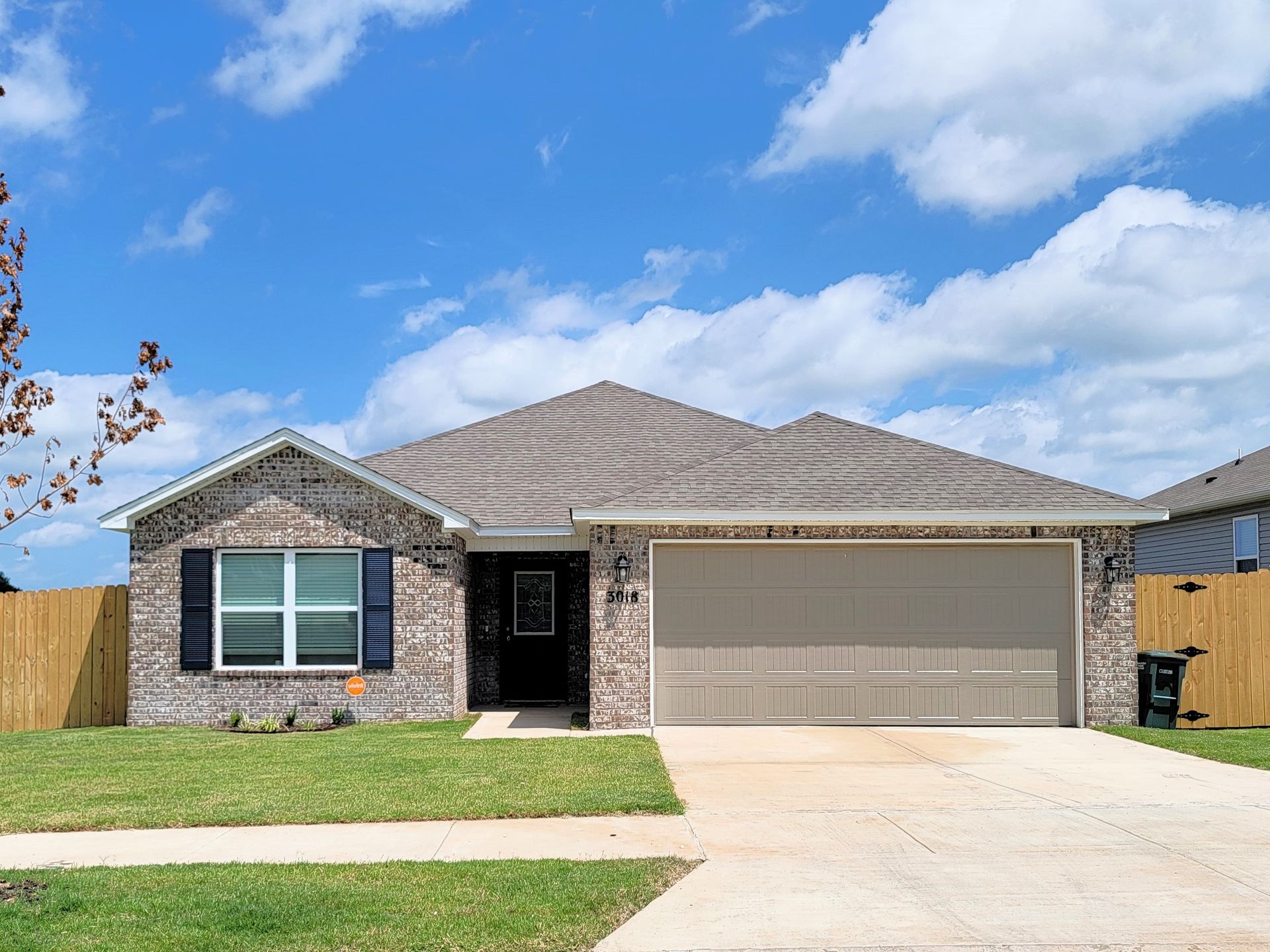 Single-story brick house with a two-car garage, front lawn, and blue sky with clouds