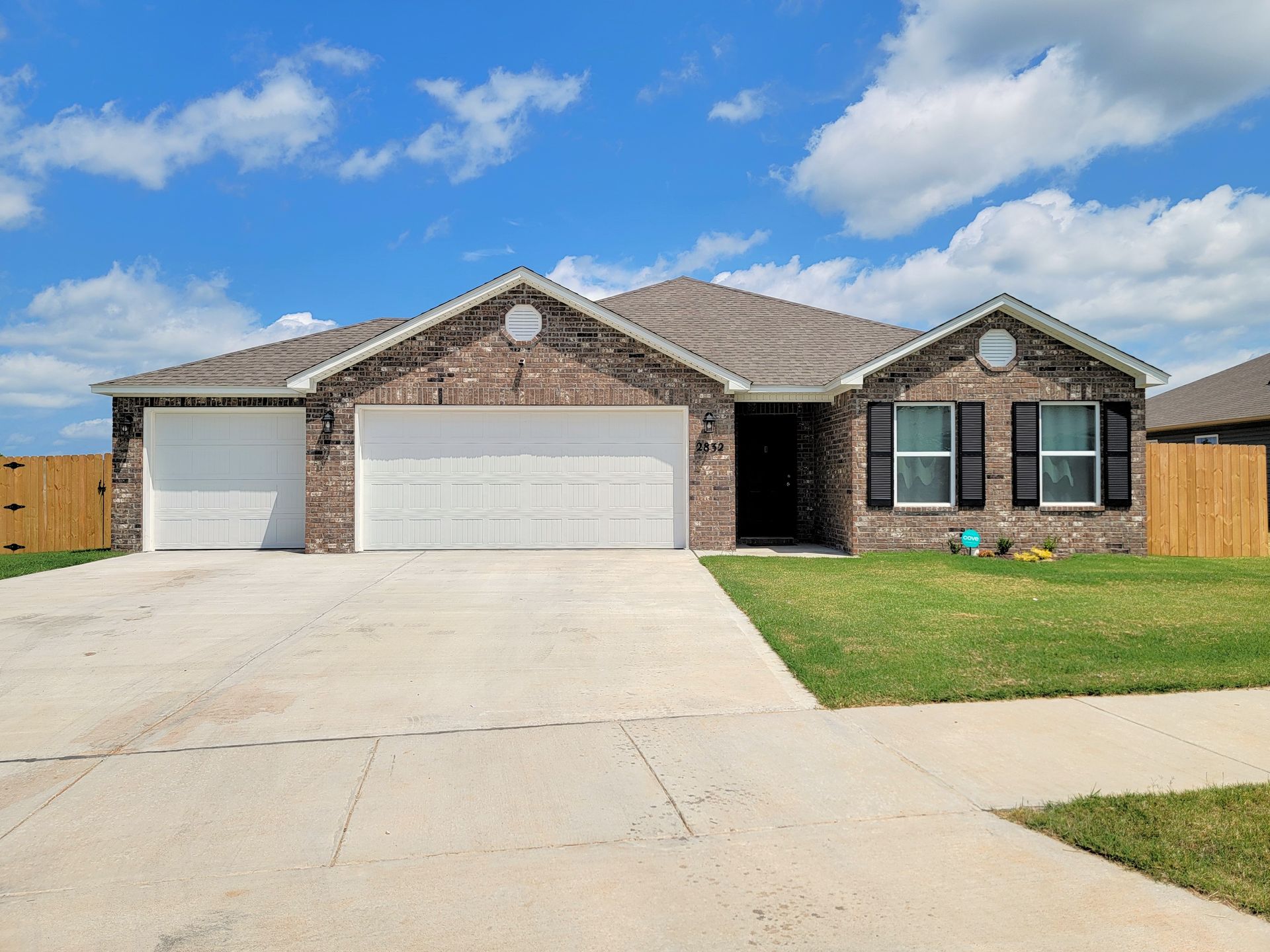 Single-story brick house with a two-car garage and wide concrete driveway under a blue sky