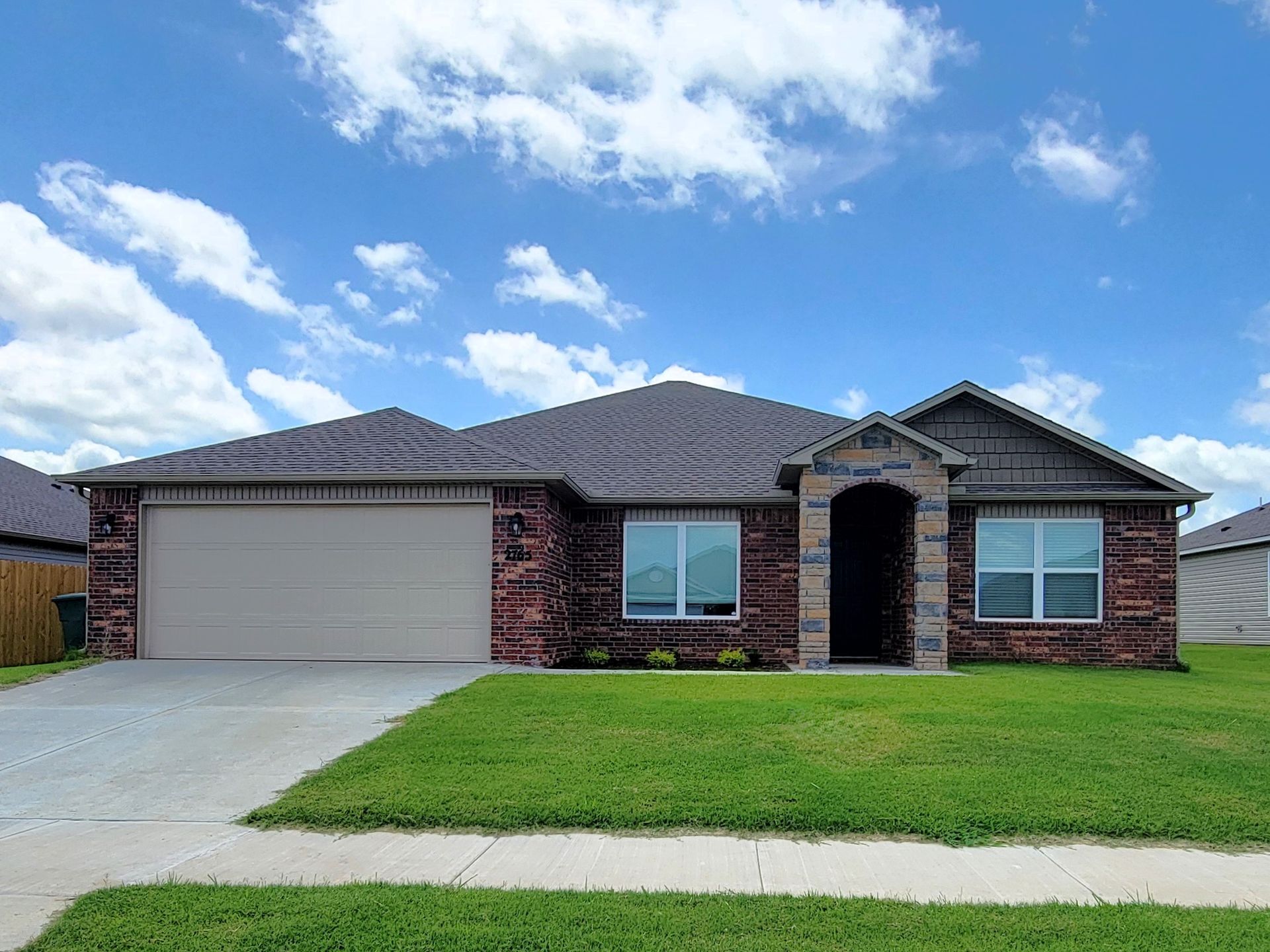 Single-story brick house with a two-car garage, front lawn, and cloudy blue sky