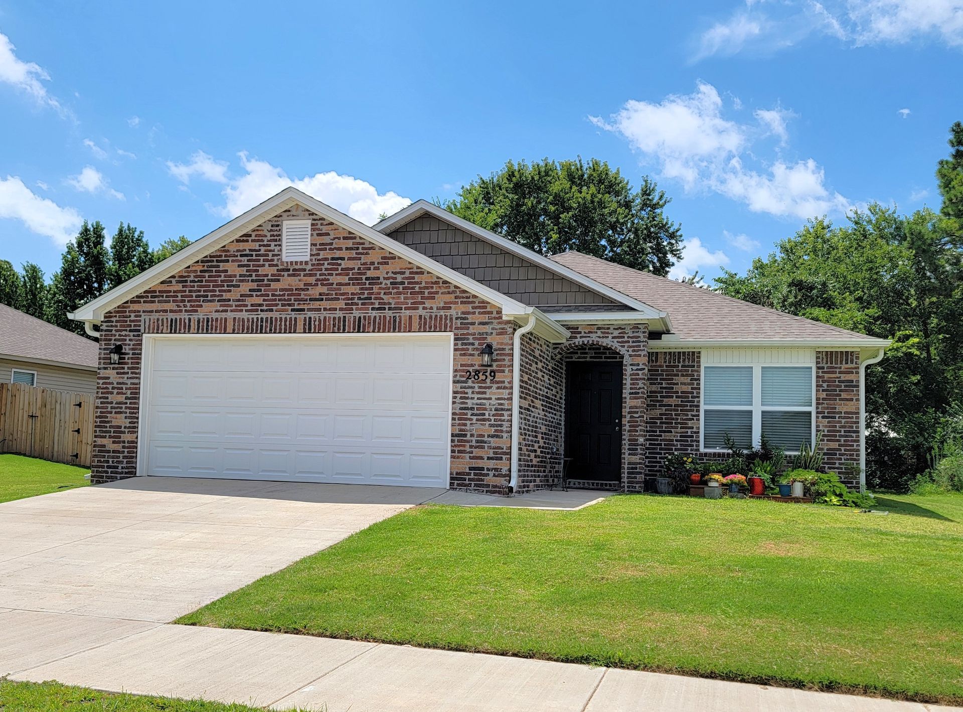 Single-story brick house with white garage door, front lawn, and blue sky