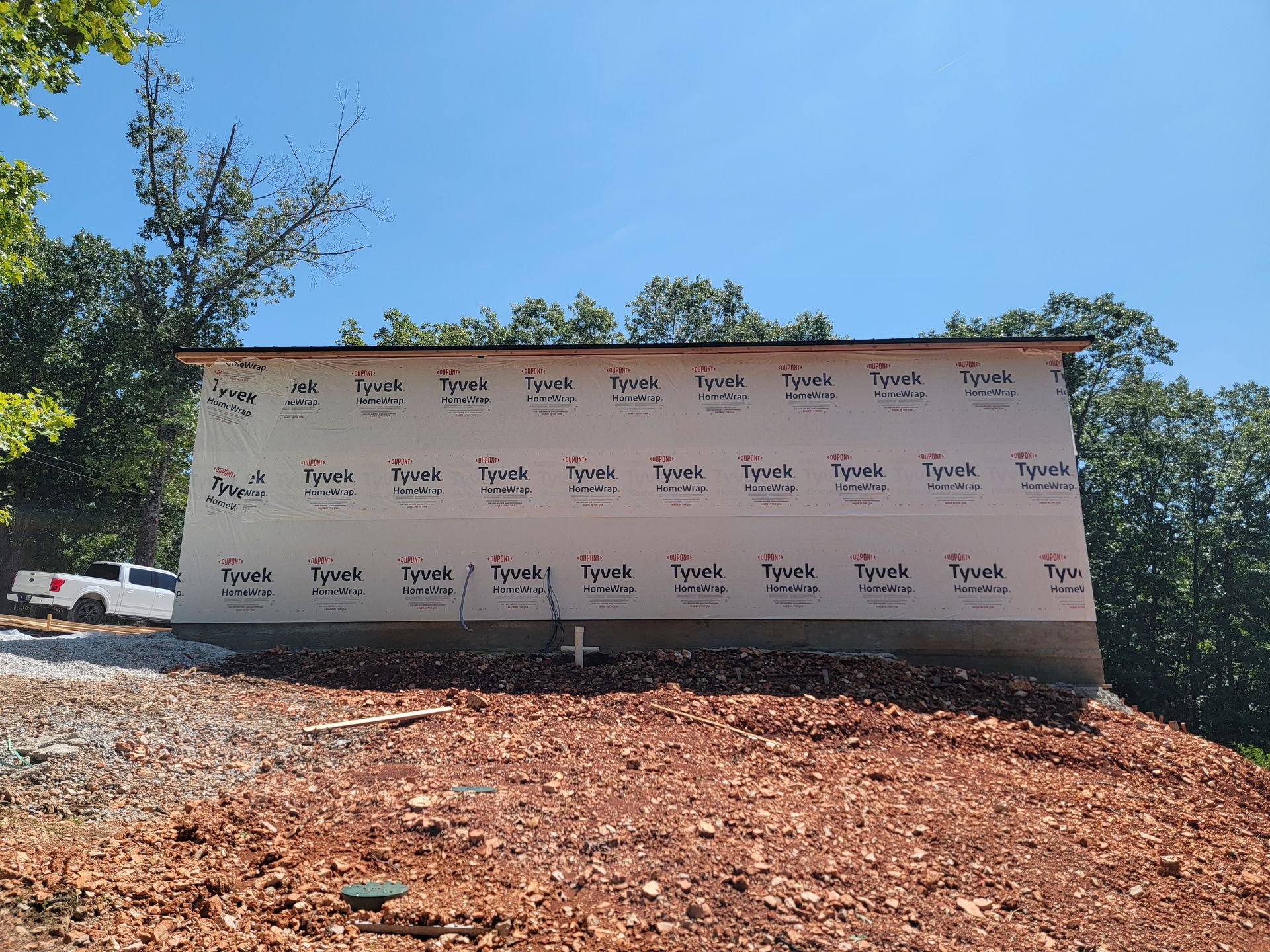 Blank white construction site sign on a dirt slope under a clear blue sky, with trees in the background
