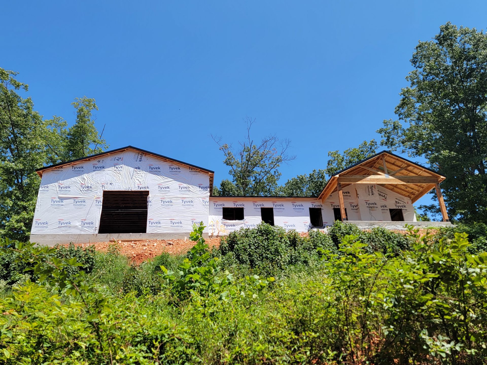 Small white house with a red roof on a green hillside under a clear blue sky