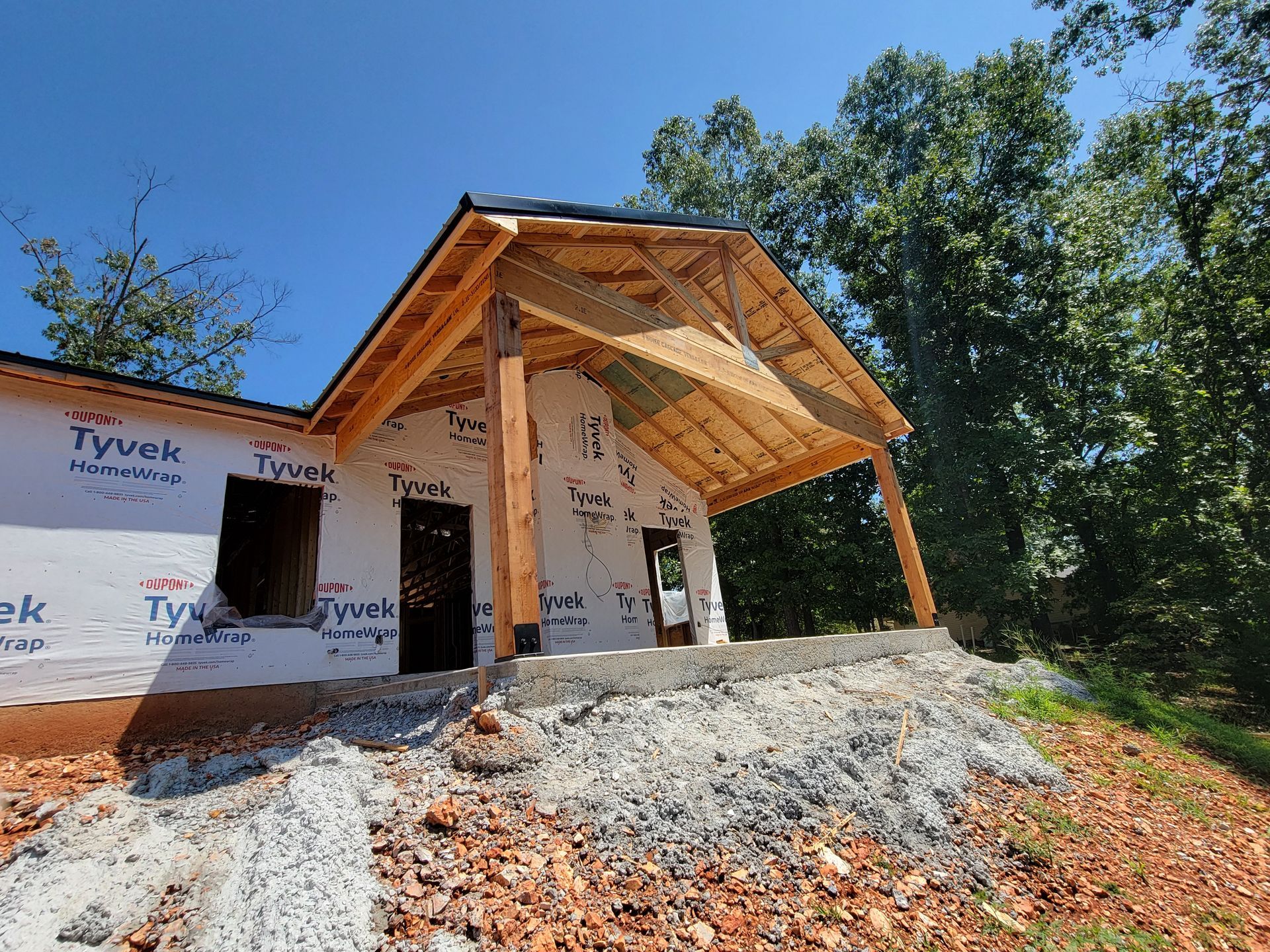 Partially built house with wood porch framing and Tyvek wrap on a rocky site under a blue sky