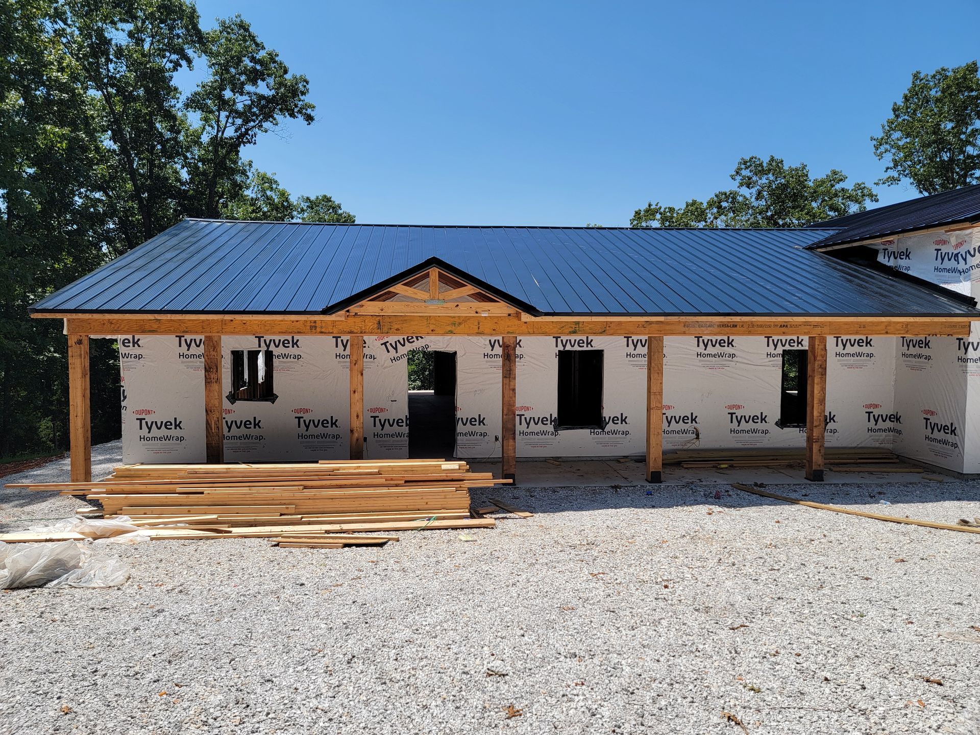Partially built single-story house with blue metal roof, unfinished porch, and gravel foreground