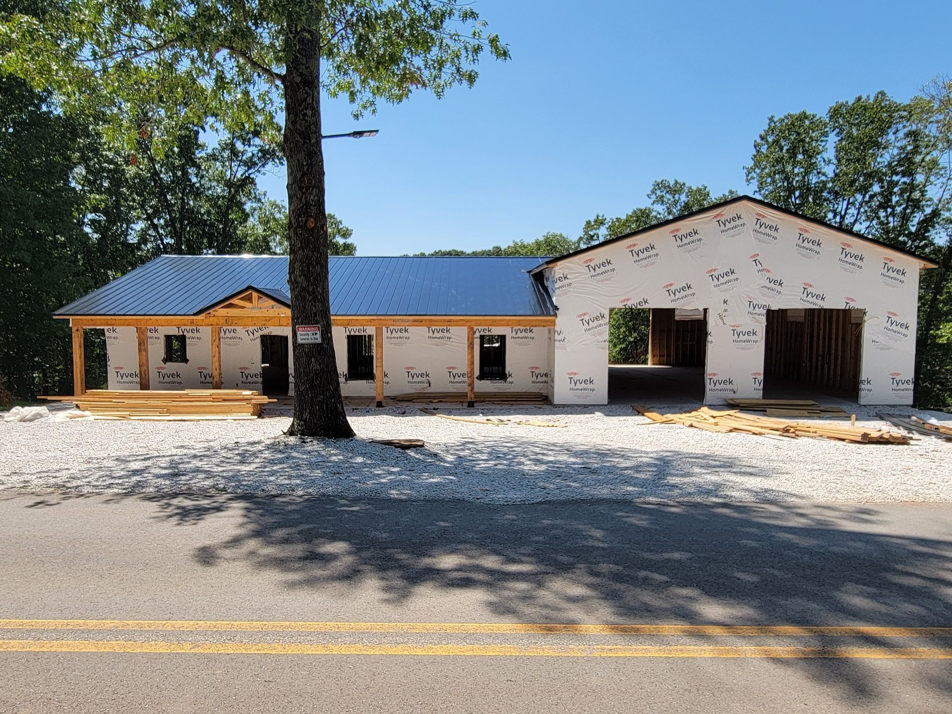 Low white building with blue metal roof, brick columns, and a gravel parking lot under clear sky