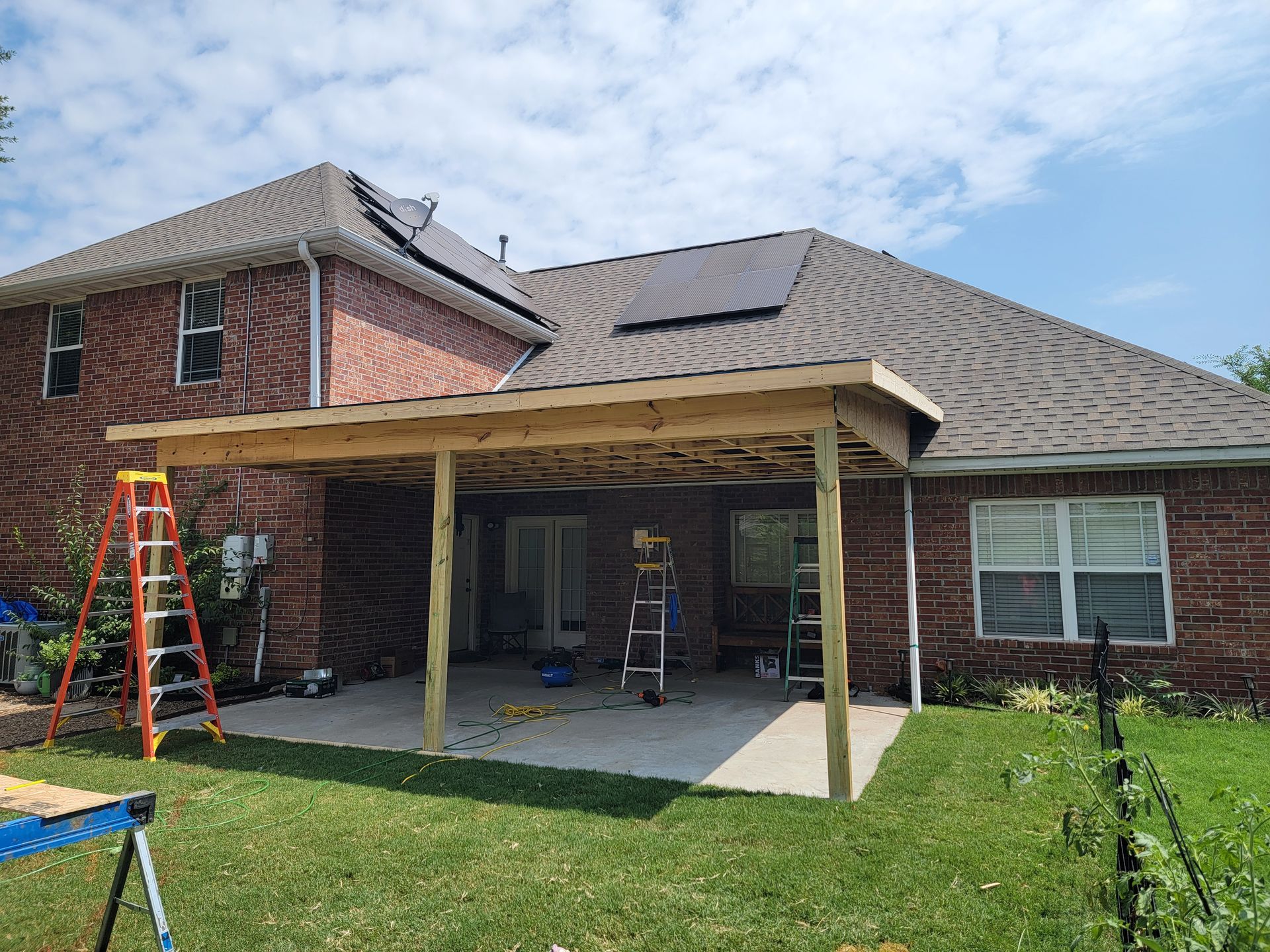 Backyard patio with brick house, covered porch, and an orange ladder on the grass