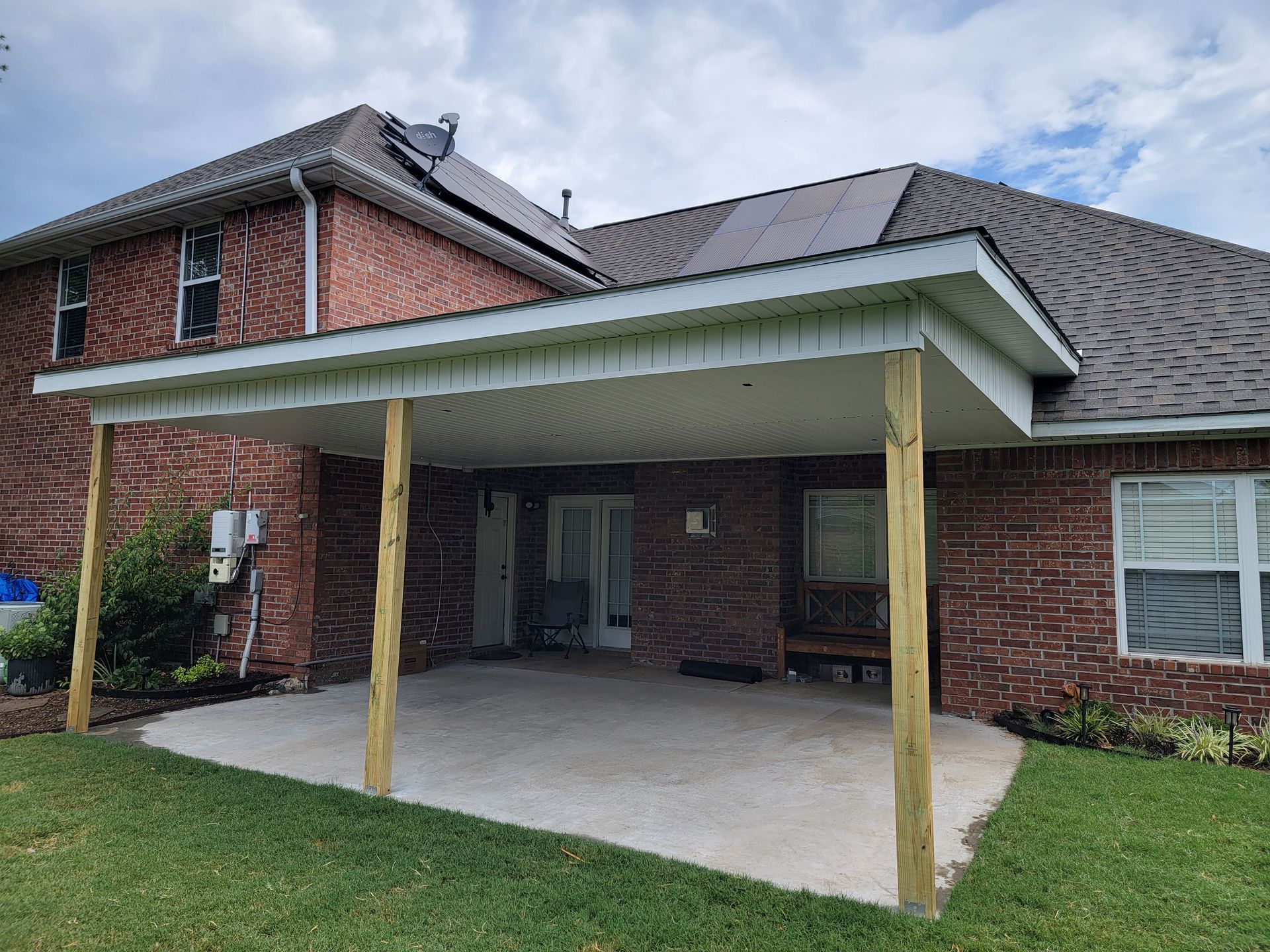 Covered brick patio with a metal roof and wooden posts beside a house